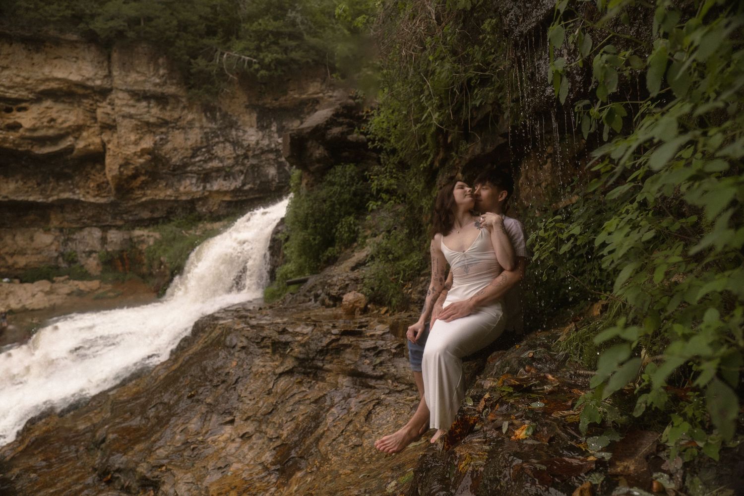 a couple in white sit near a waterfall