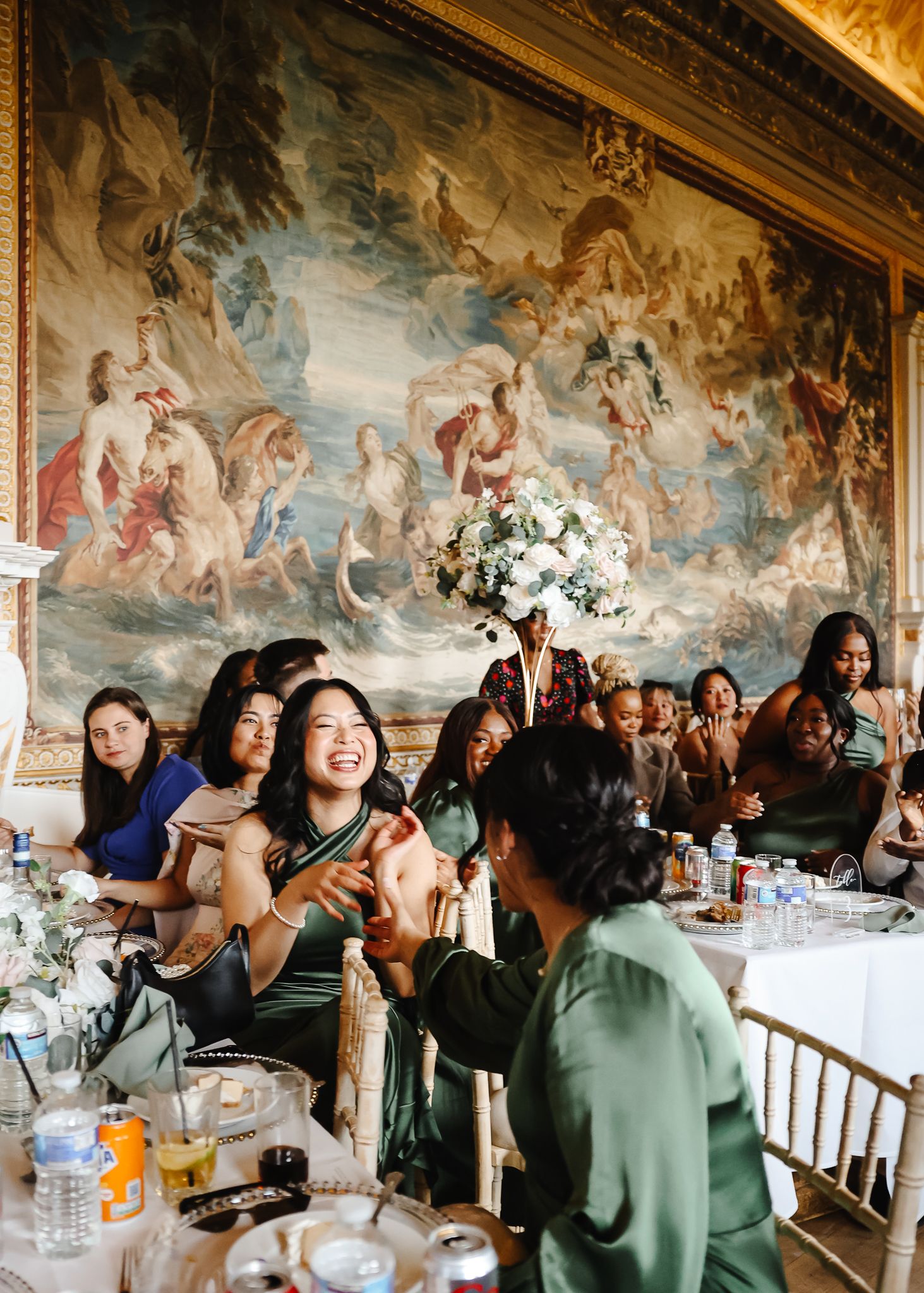 People gathered at a long dining table in an ornate room with classical ceiling murals during a formal event.