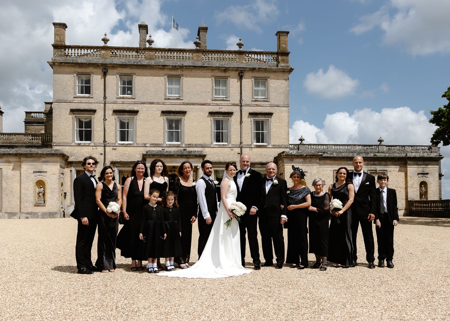 Wedding party poses in formal attire against classical architecture of stately home.