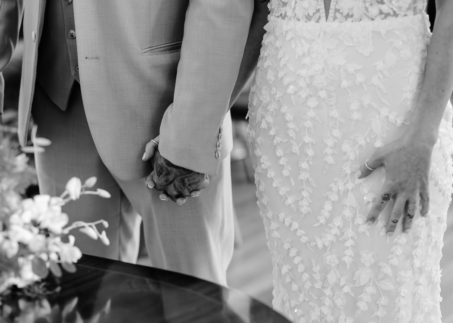 Black and white photo showing hands holding each other in a wedding ceremony setting.