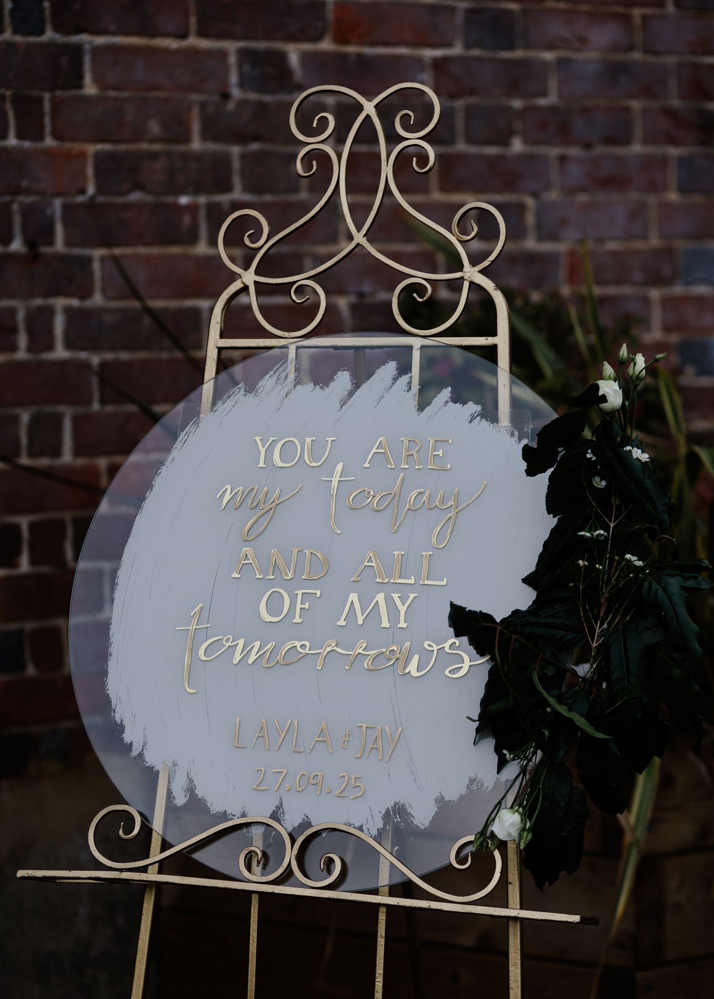 Elegant white and gold wedding signs with ornate scrollwork frames displayed against a rustic brick wall backdrop.