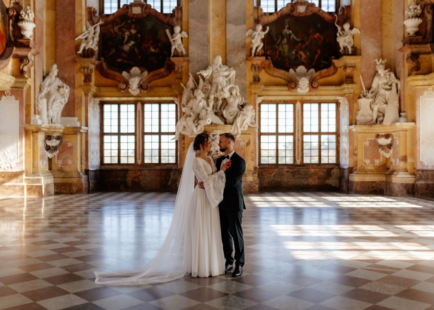 A panoramic view of an elegant ballroom with ornate chandeliers, marble columns and sunlight streaming through tall windows.