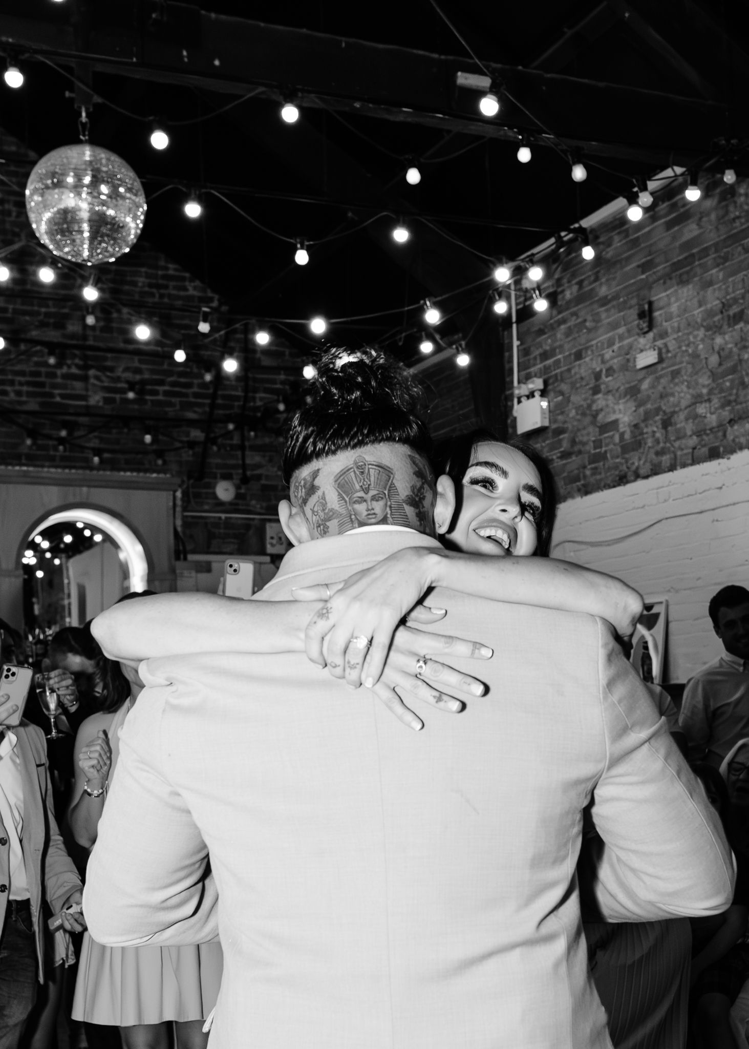 Wedding guests embracing and celebrating on the dance floor under string lights.