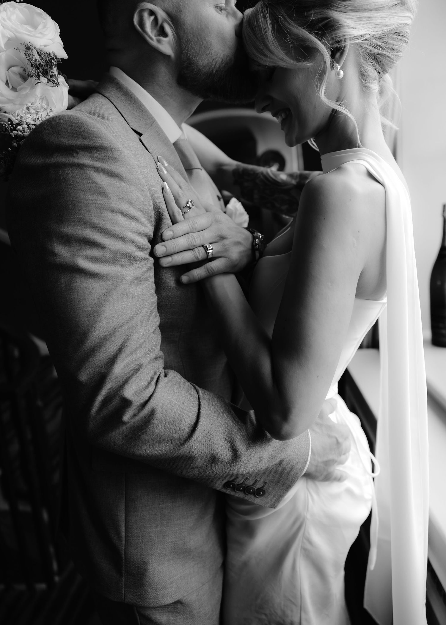 Black and white photo of a couple sharing a romantic kiss at their wedding, bride in elegant gown, groom in gray suit.