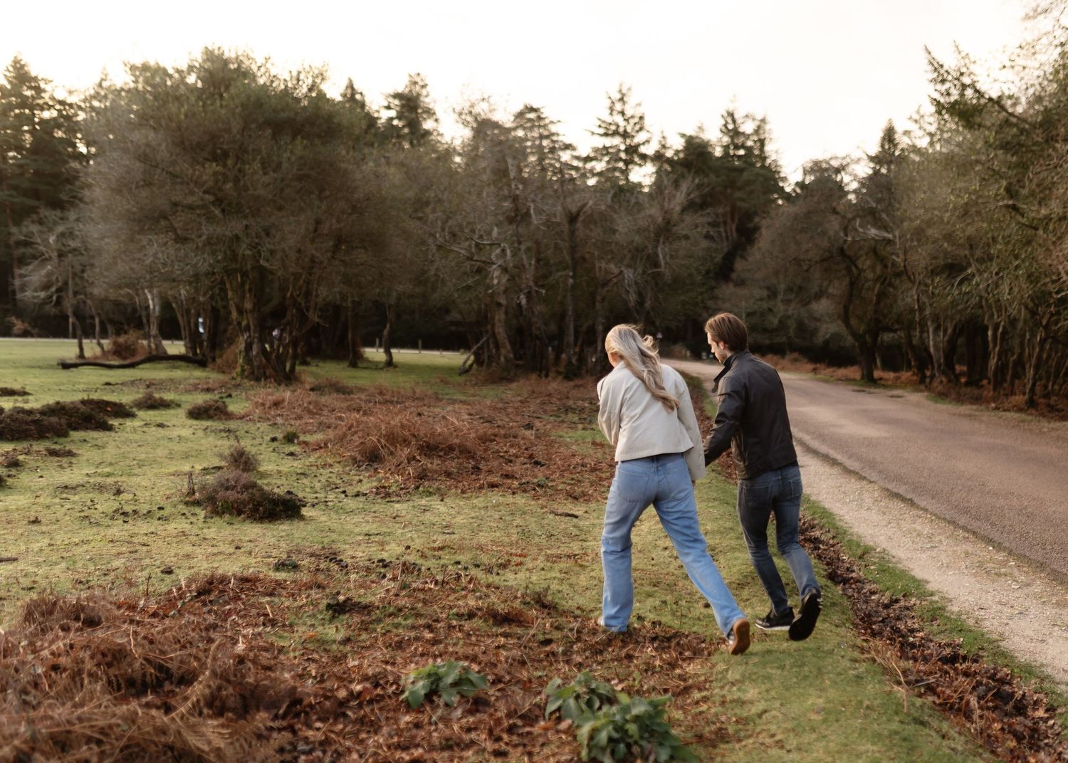 Couple walking hand in hand along a countryside road surrounded by lush green trees and ferns.