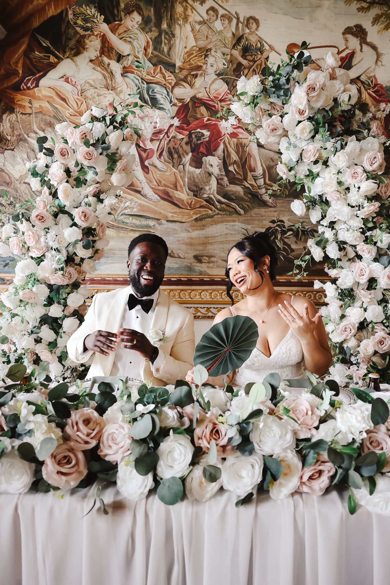 Elegant wedding reception decor featuring cascading white and blush floral arrangements against a classical fresco backdrop.