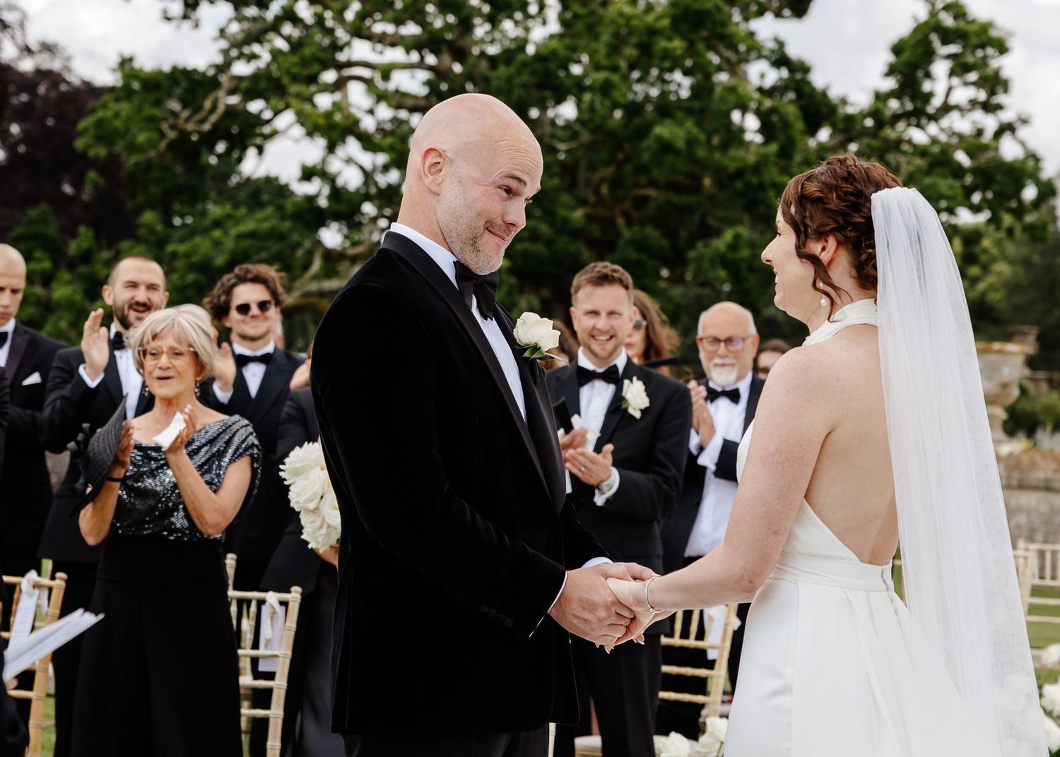 Intimate outdoor wedding ceremony with guests seated on chiavari chairs and white floral decorations.