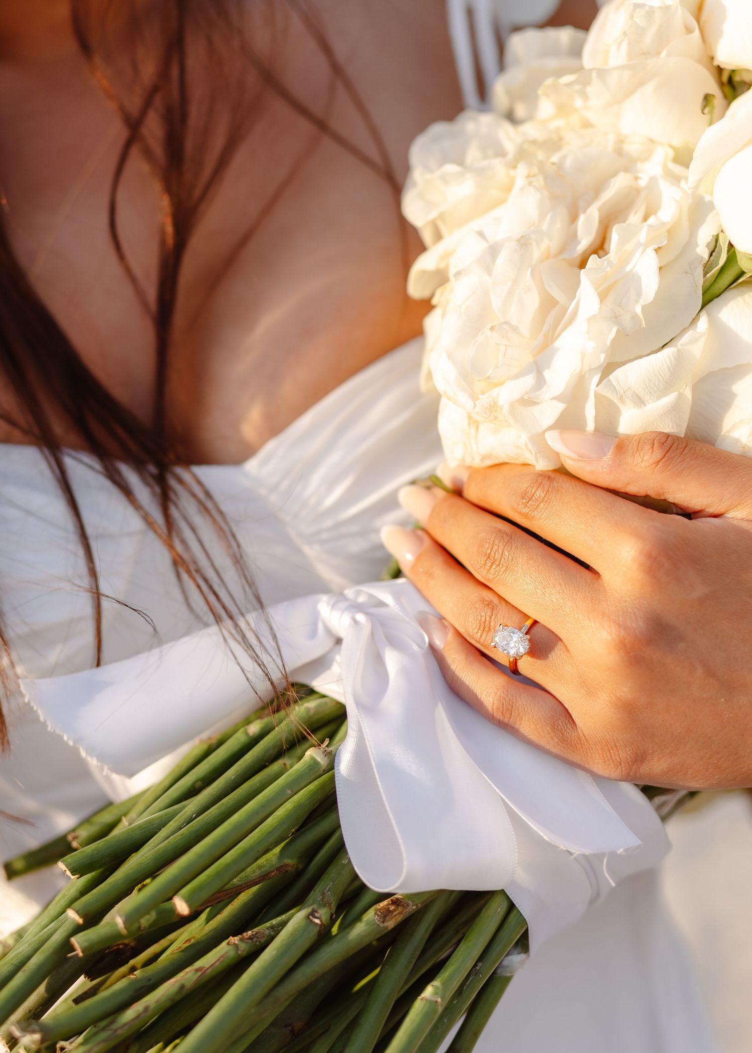 Bride holding white floral bouquet with bamboo stems, showcasing diamond engagement ring on wedding day.