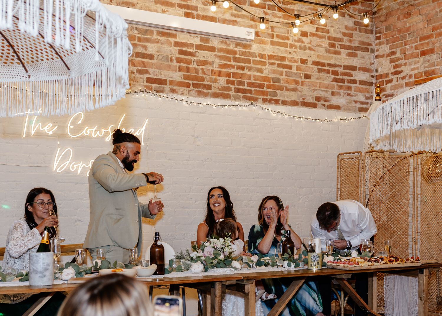 Wedding guests mingle and celebrate in a rustic brick-walled venue with elegant table settings and decor.