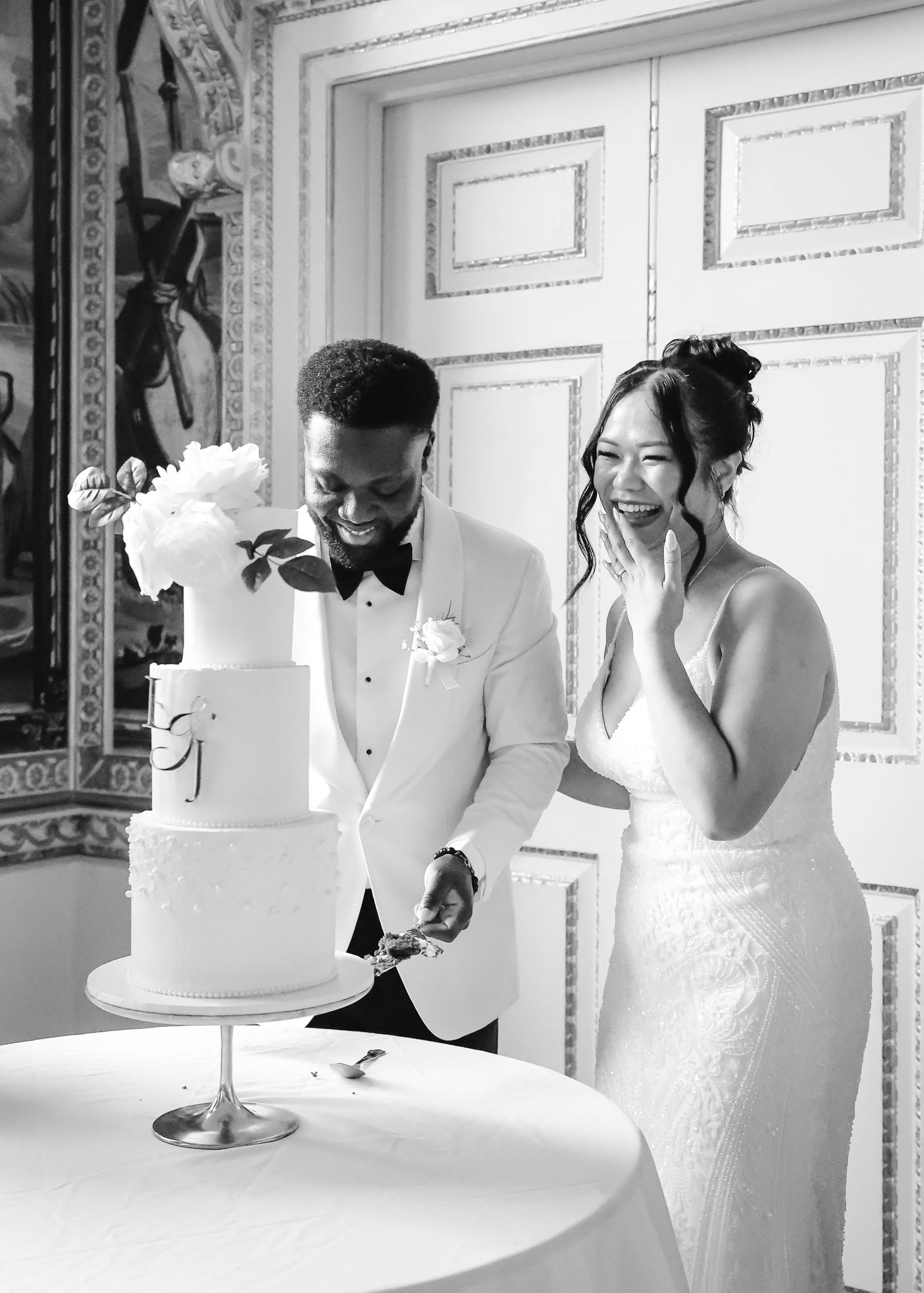 A joyful couple shares a candid moment while cutting their elegant white wedding cake at their reception.