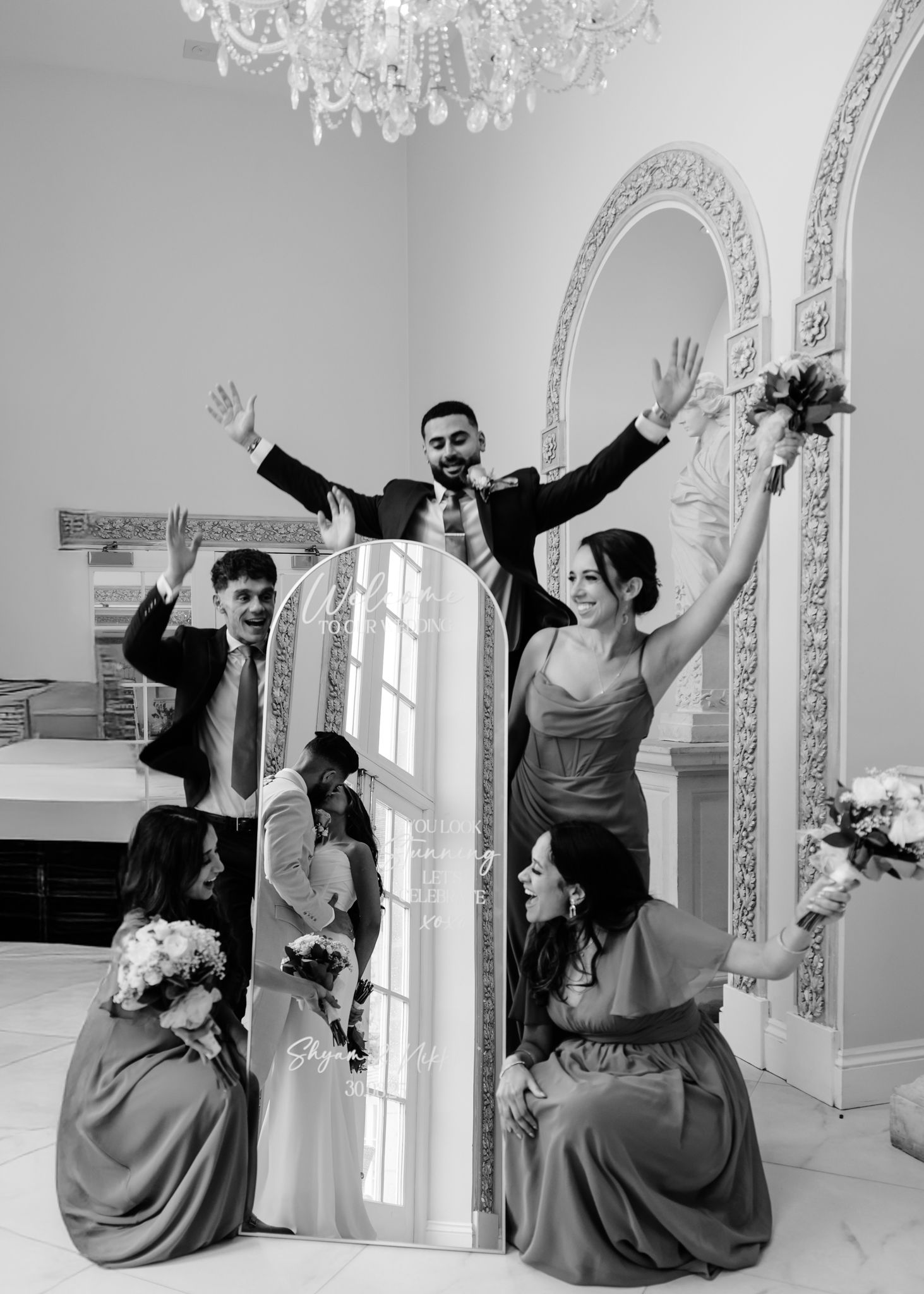 A group in matching gray dresses strikes playful poses in a bright white room with ornate architectural details.