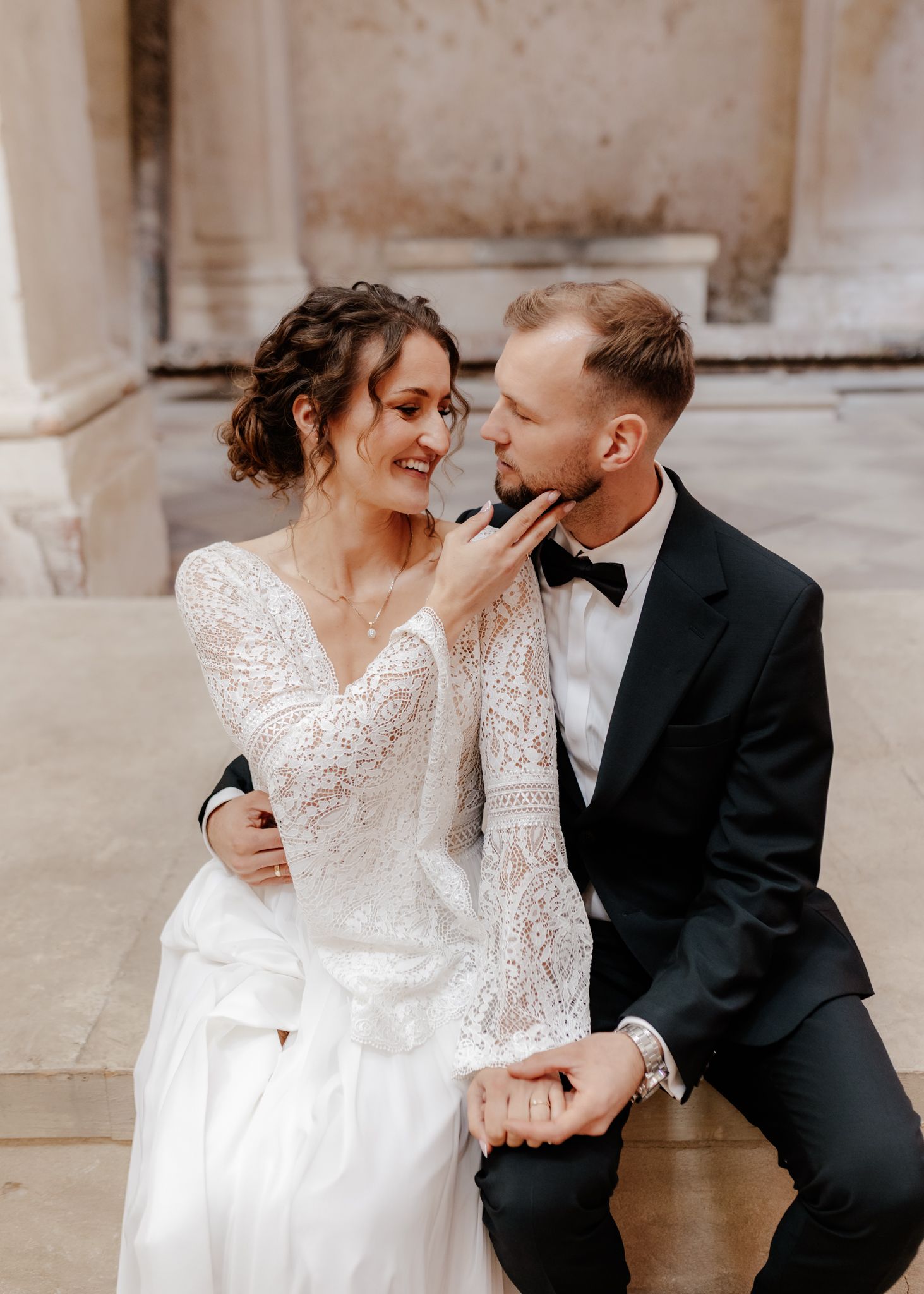 An intimate wedding portrait showing tender moments in a historic stone building setting.