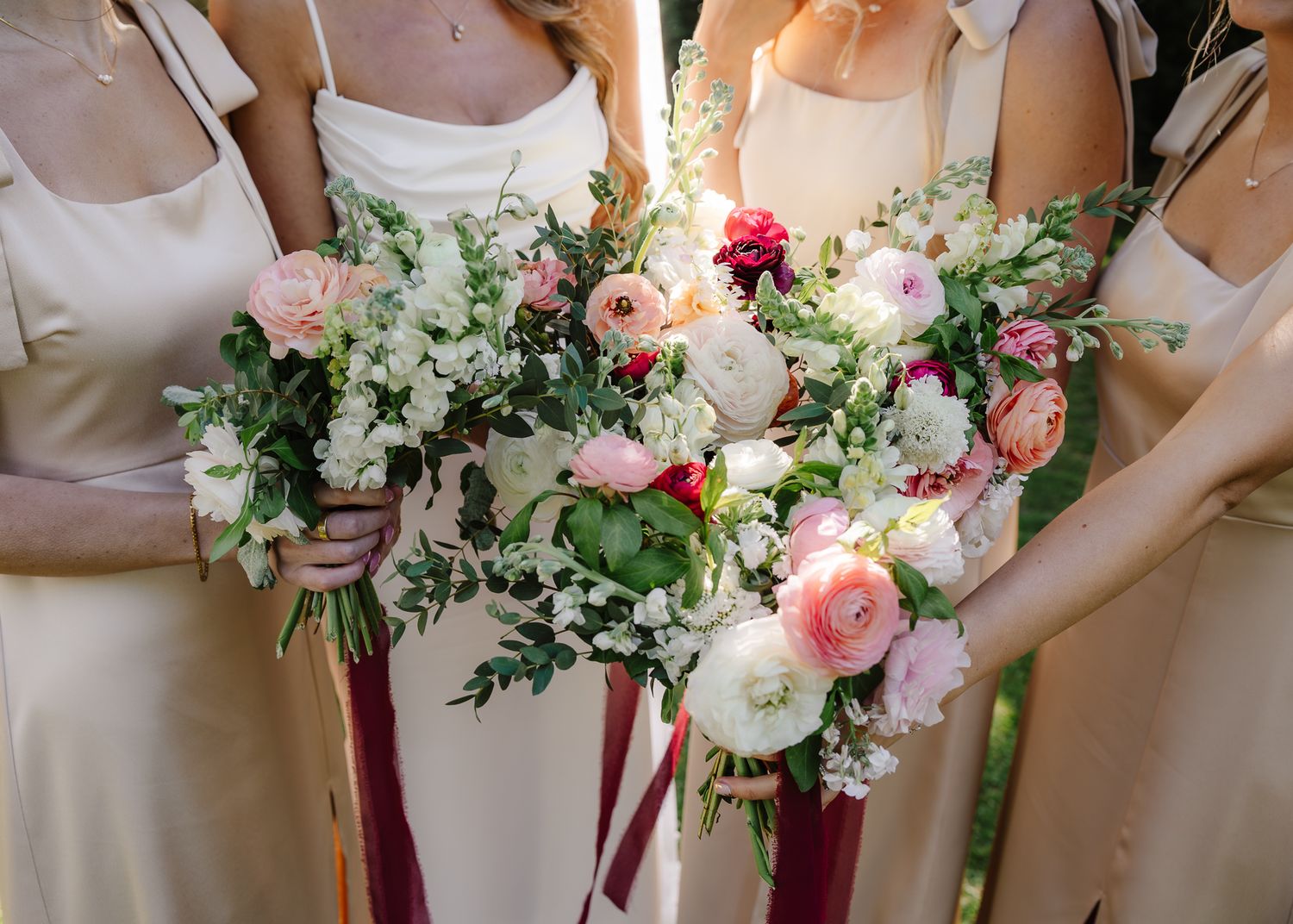 Bridesmaids hold beautiful bouquets featuring pink and white flowers with flowing ribbons.