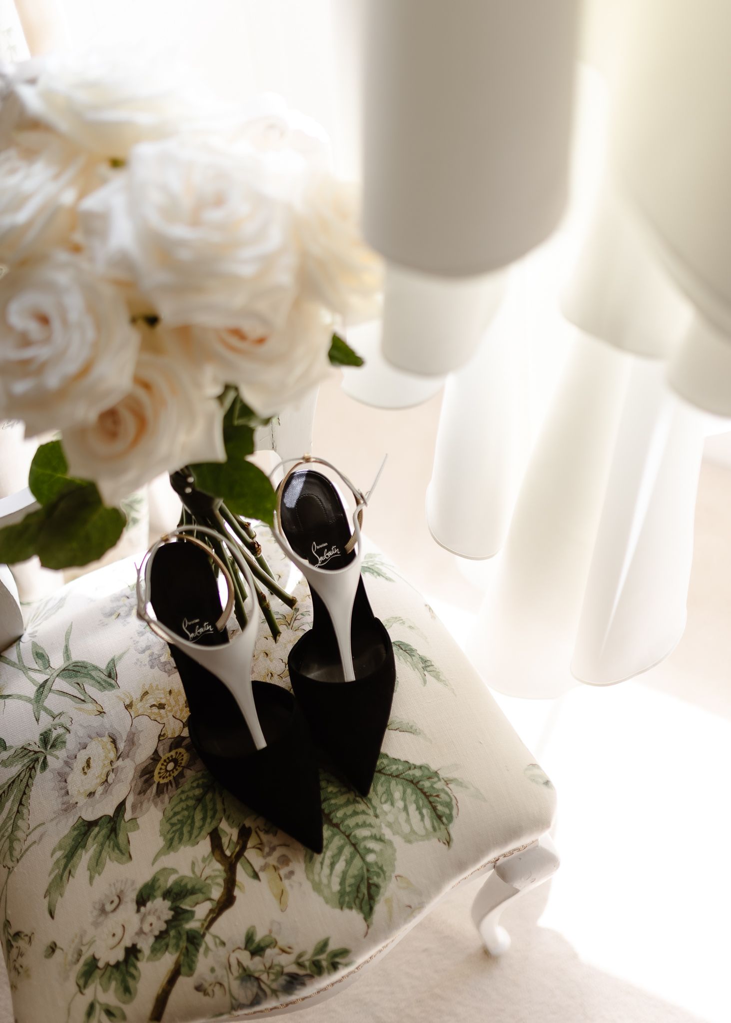 Elegant black and white wedding shoes nestled among delicate white roses and greenery on a light surface.