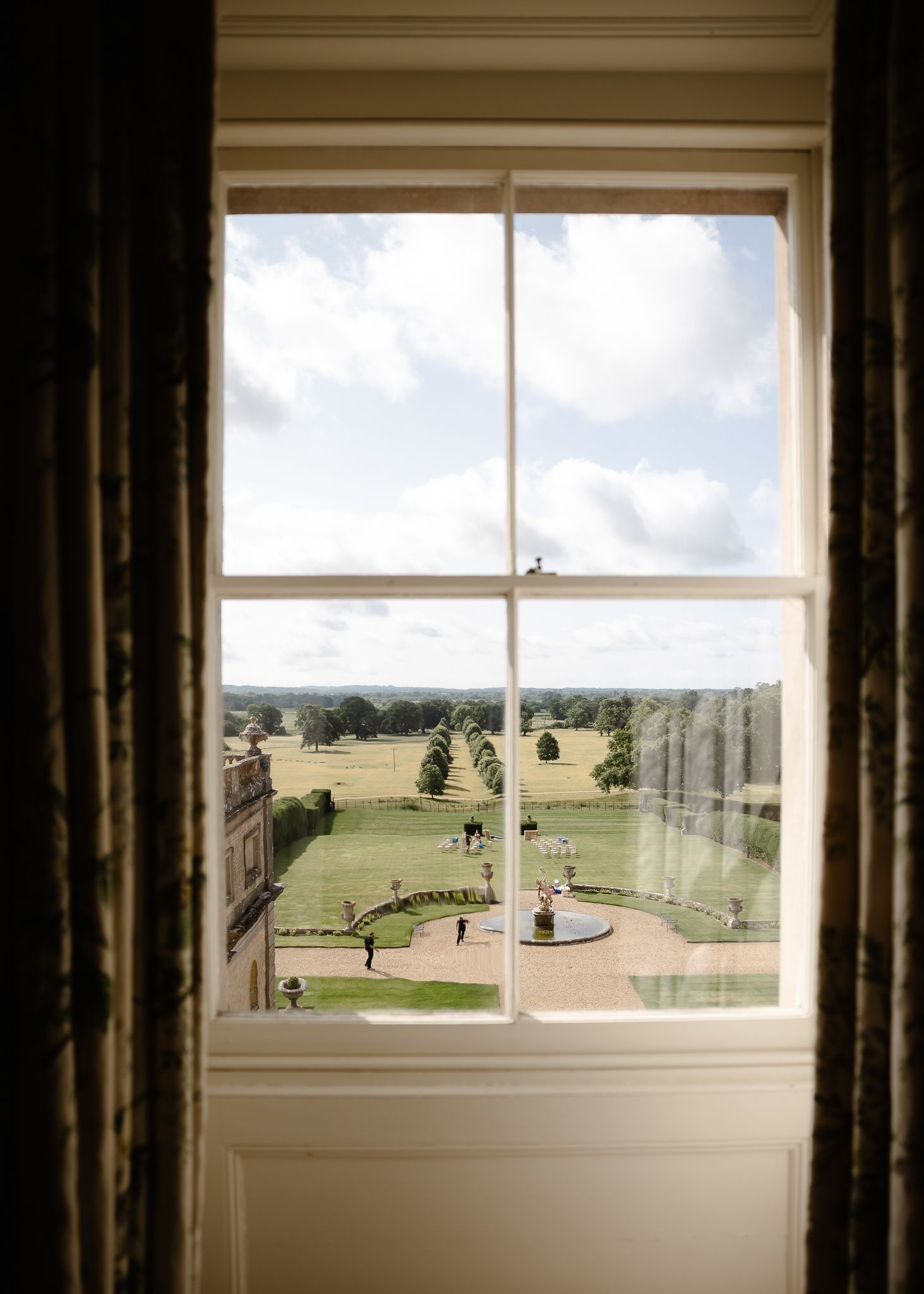 A panoramic view through a window shows a manicured garden landscape with green fields stretching to the horizon.