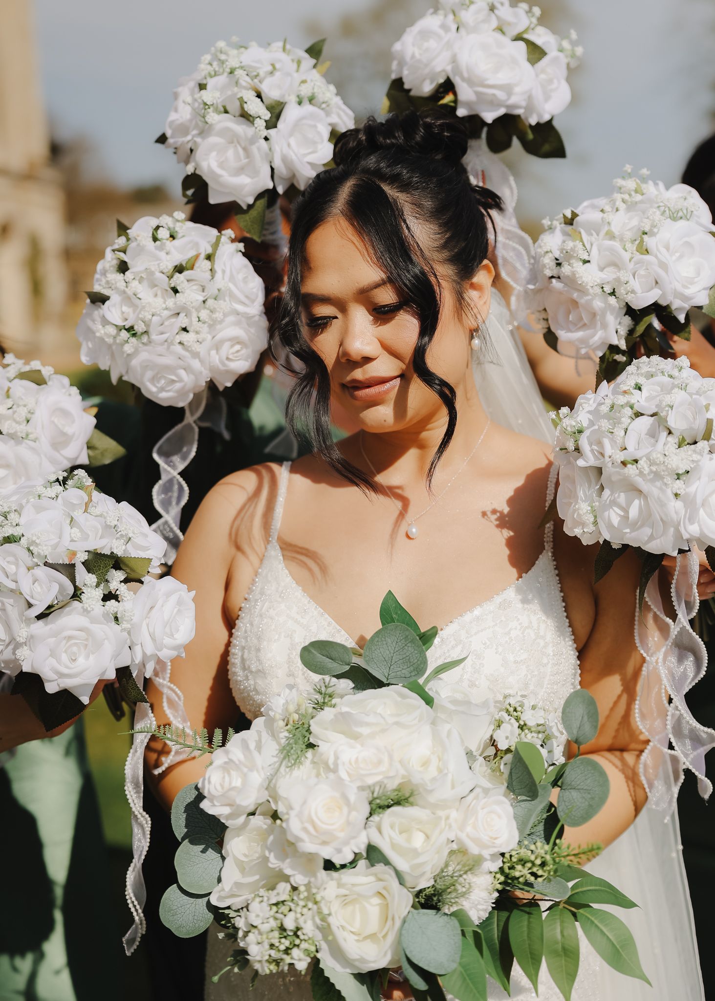 A bride in a white gown poses among cascading white flowers and greenery in an elegant wedding setting.