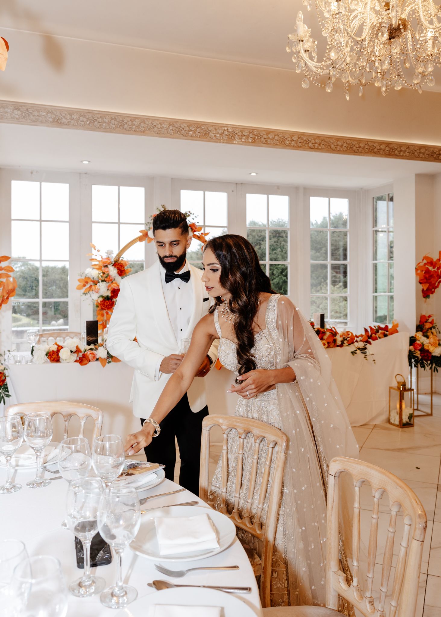 Elegant wedding reception venue with white chairs and autumn decor featuring crystal chandeliers and large windows.