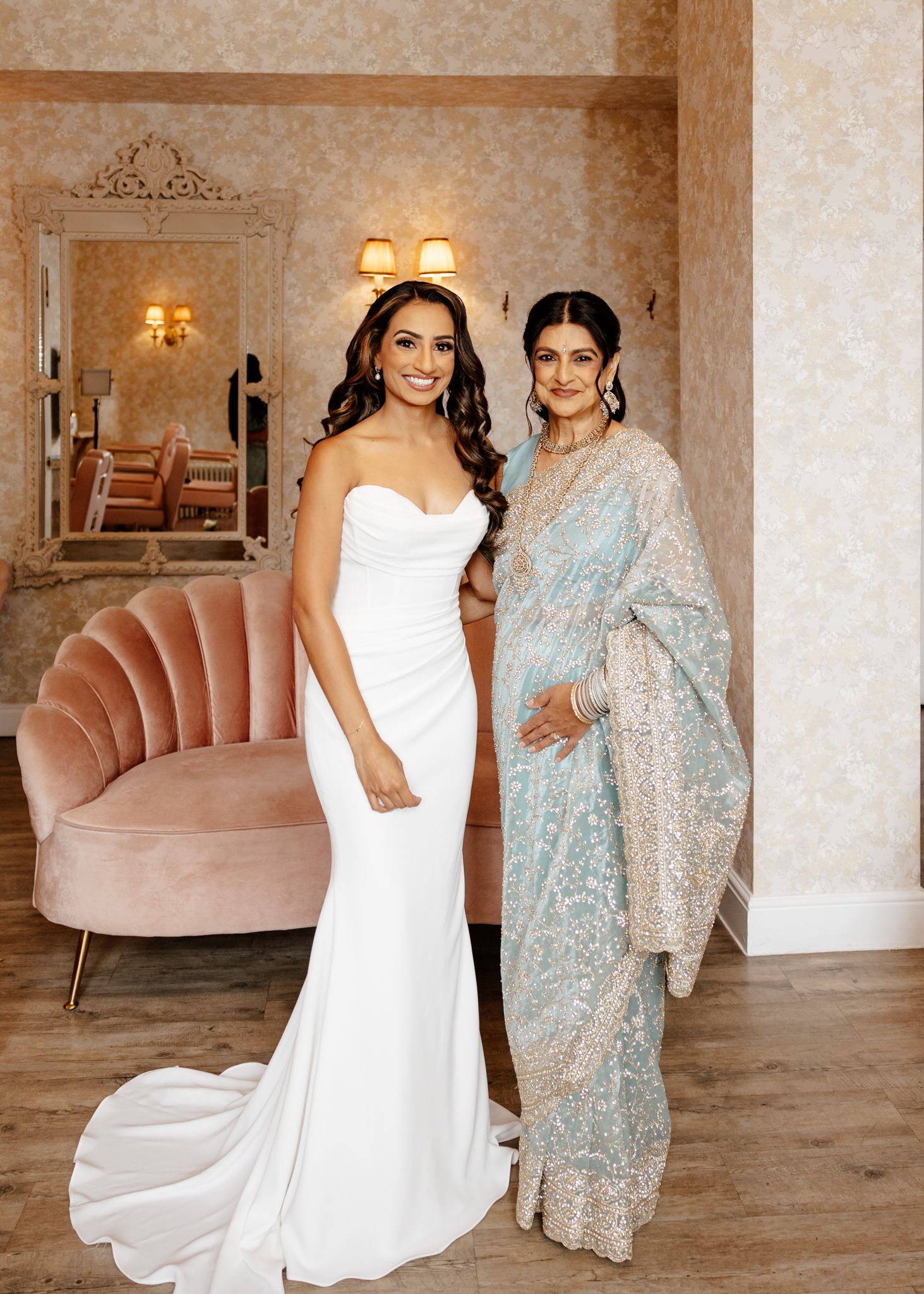 Two people pose together in formal attire, one wearing a white gown and the other in a sparkly light blue dress.