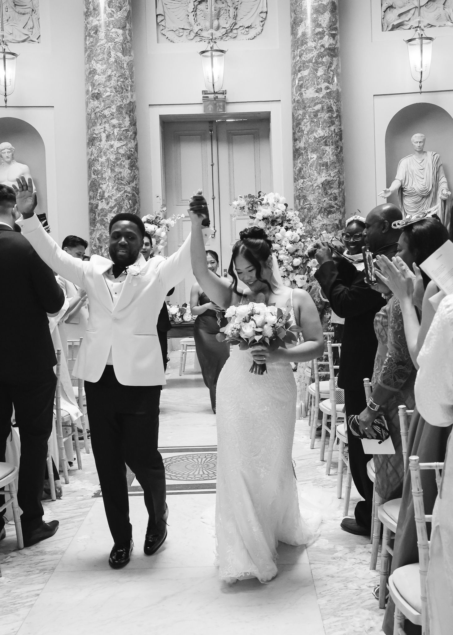 Wedding guests dance together in a grand ballroom with marble columns and elegant decor during a reception celebration.