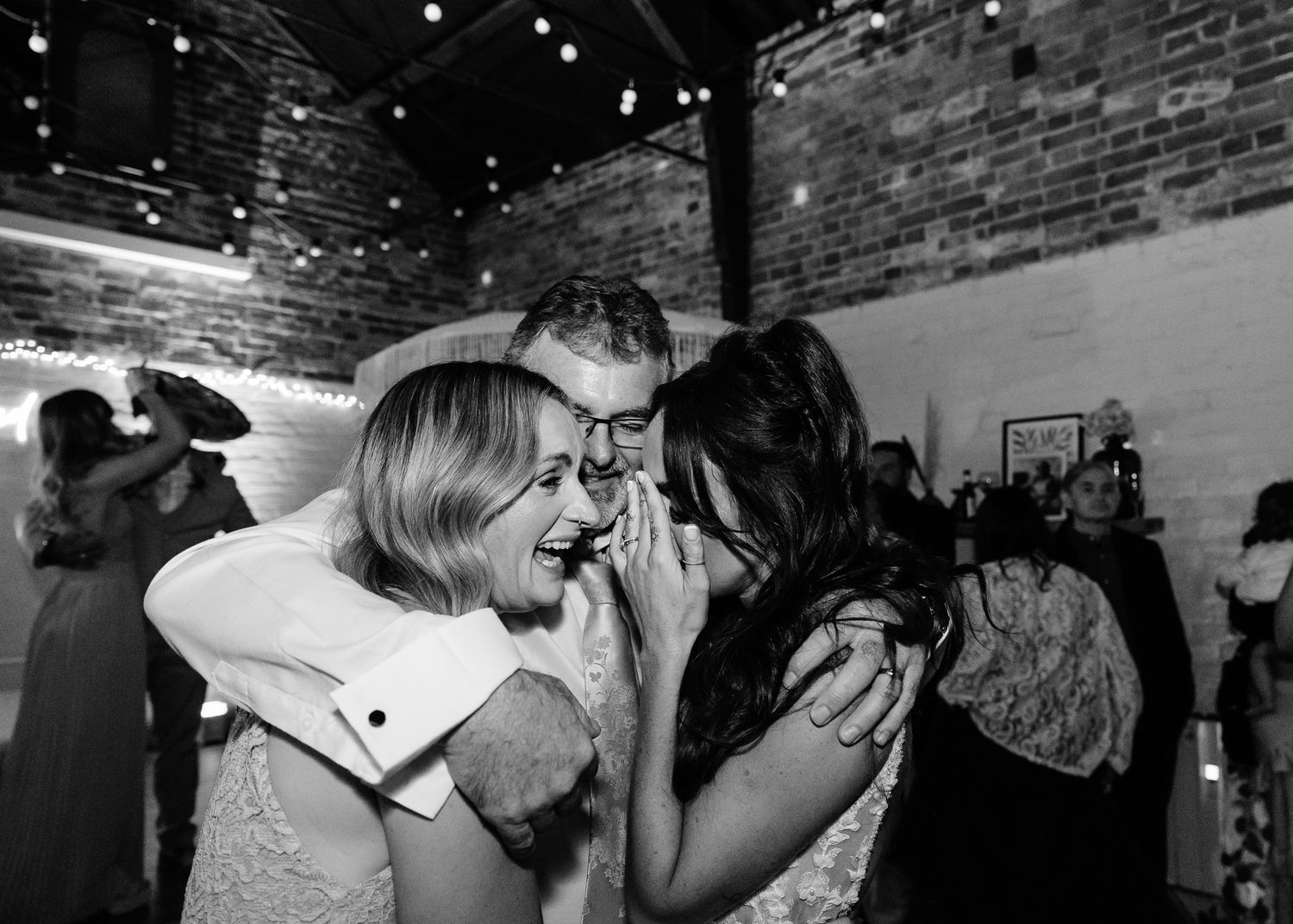 Couples dancing together at a dimly lit wedding reception with string lights overhead.