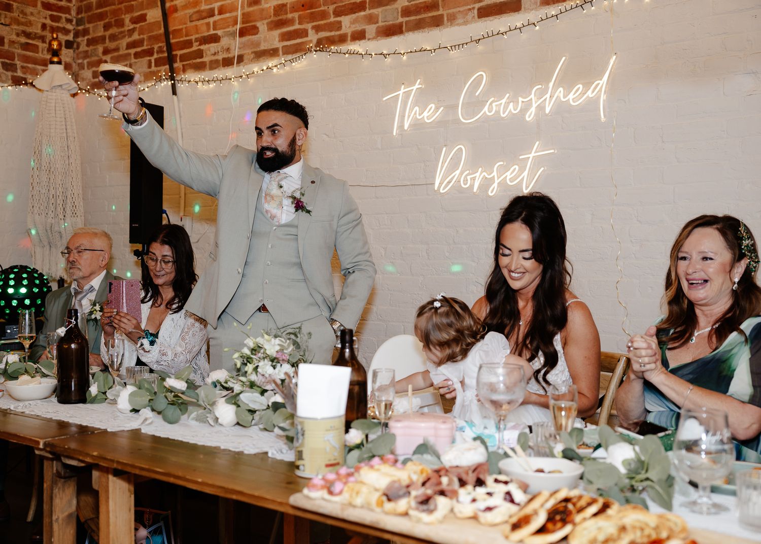 Wedding reception buffet setup with rustic brick wall backdrop and string lights overhead.
