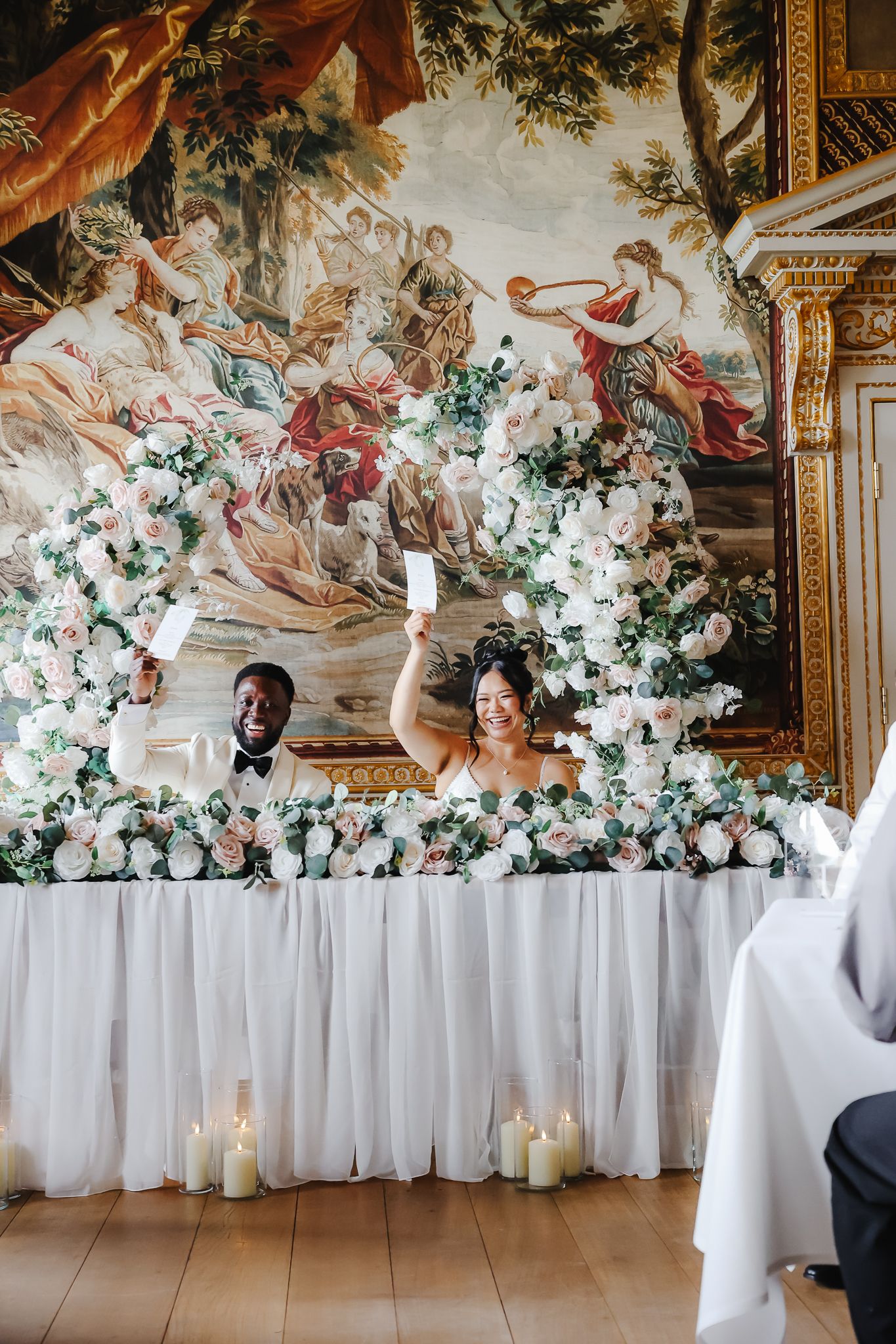 Elegant wedding reception room with ornate murals and floral arrangements along white-draped tables.