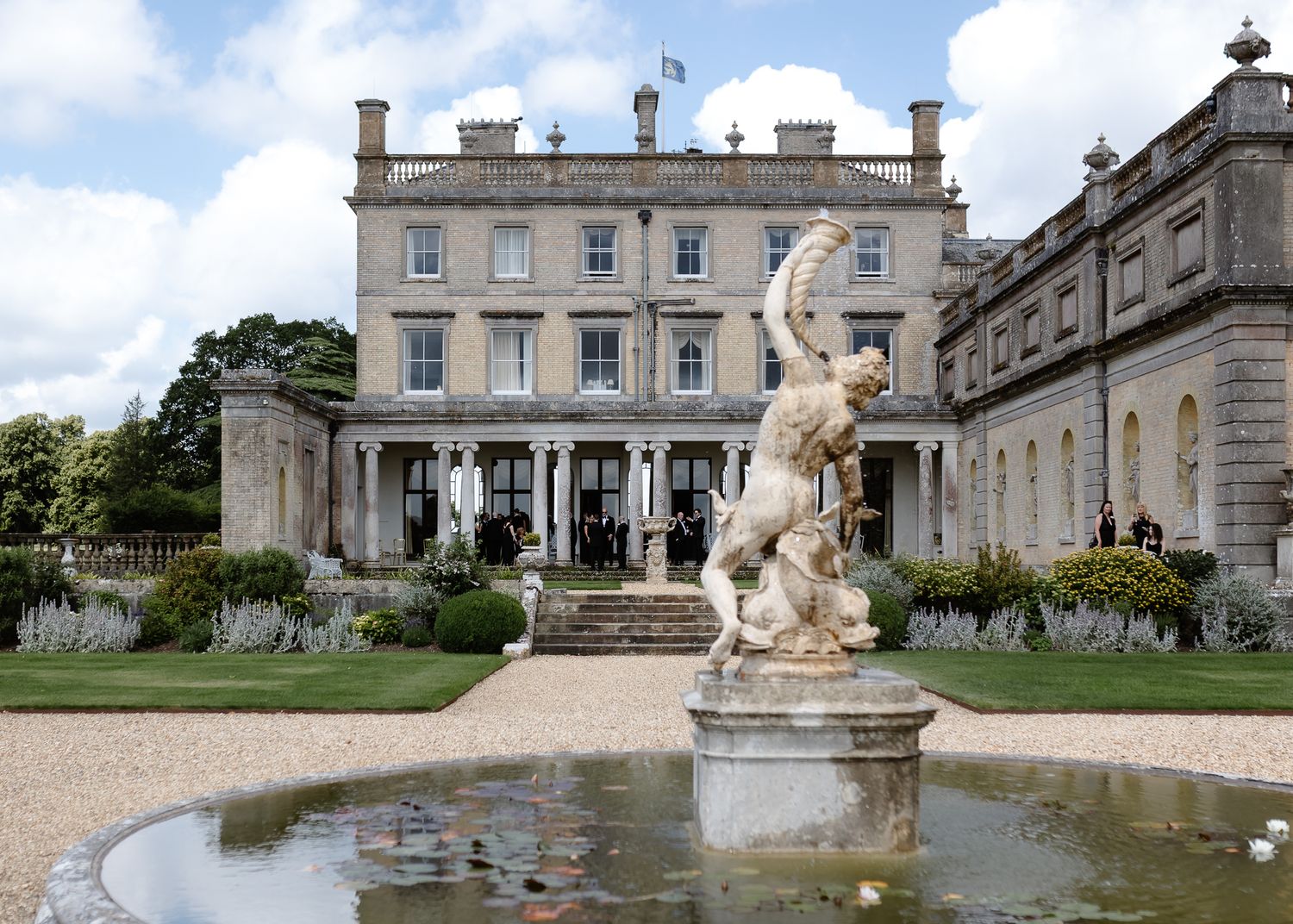 A panoramic view of a grand historic estate with manicured gardens and ornate stone fountains.