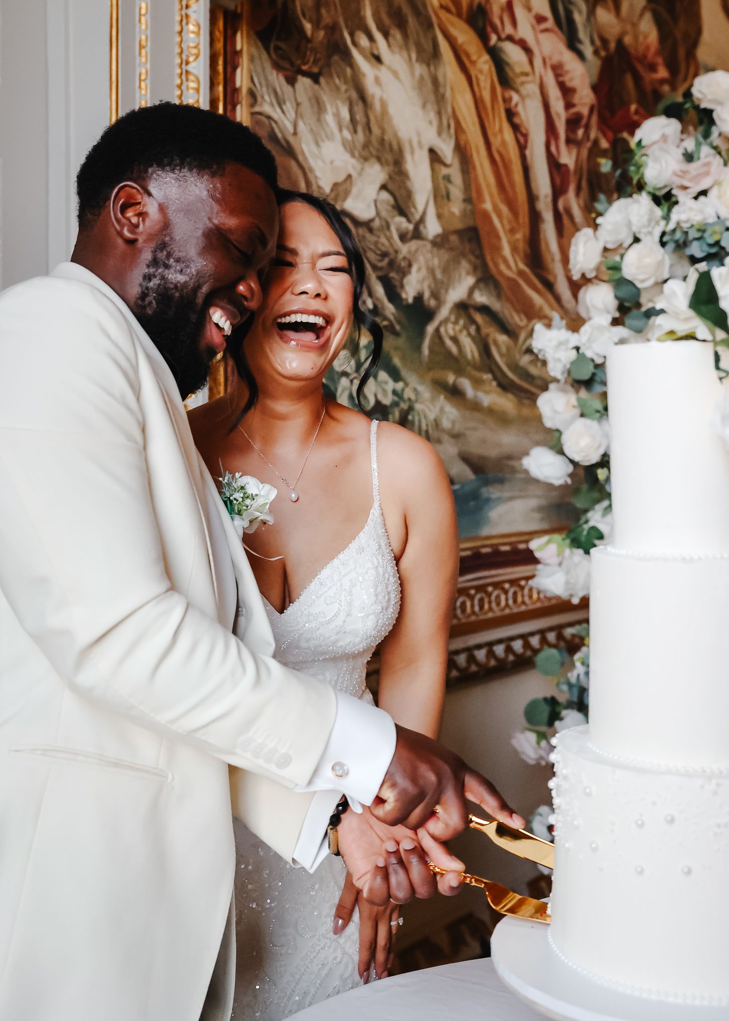 Happy newlyweds share a joyful moment while cutting their elegant white wedding cake at their reception.