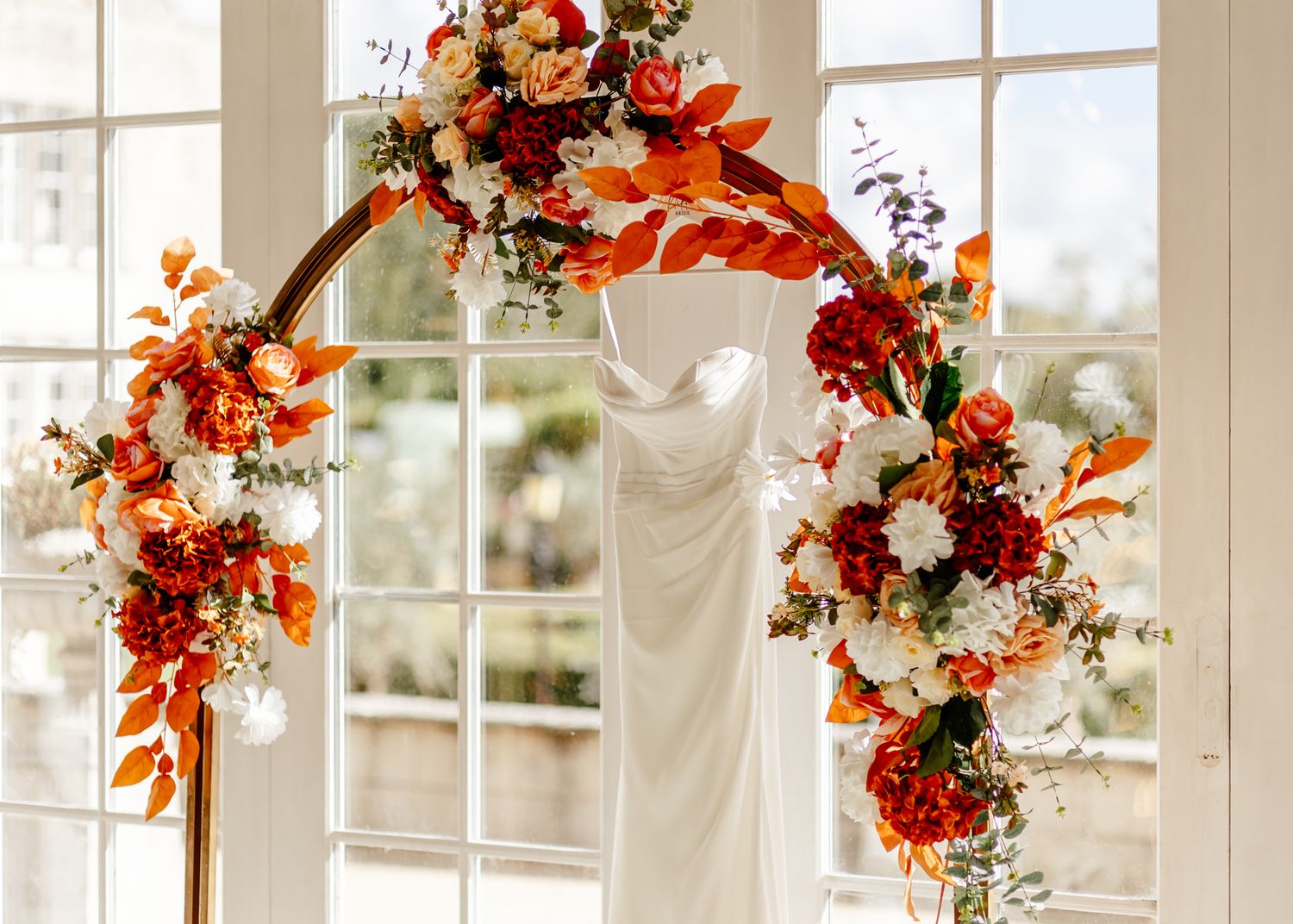 Elegant wedding arch decorated with vibrant orange and burgundy floral arrangements against white French doors.