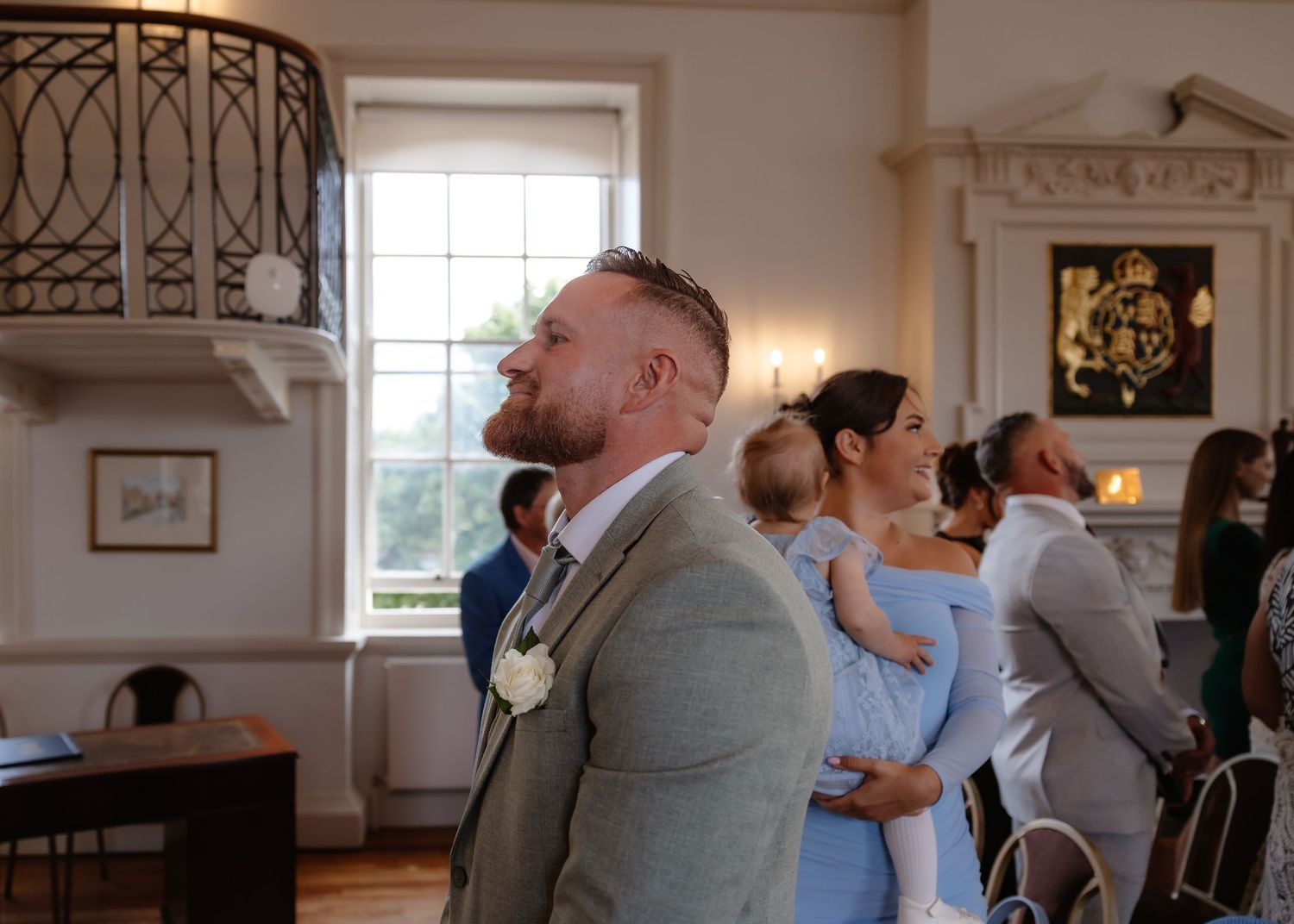 Groom in sage suit awaiting bride at wedding ceremony in elegant venue.