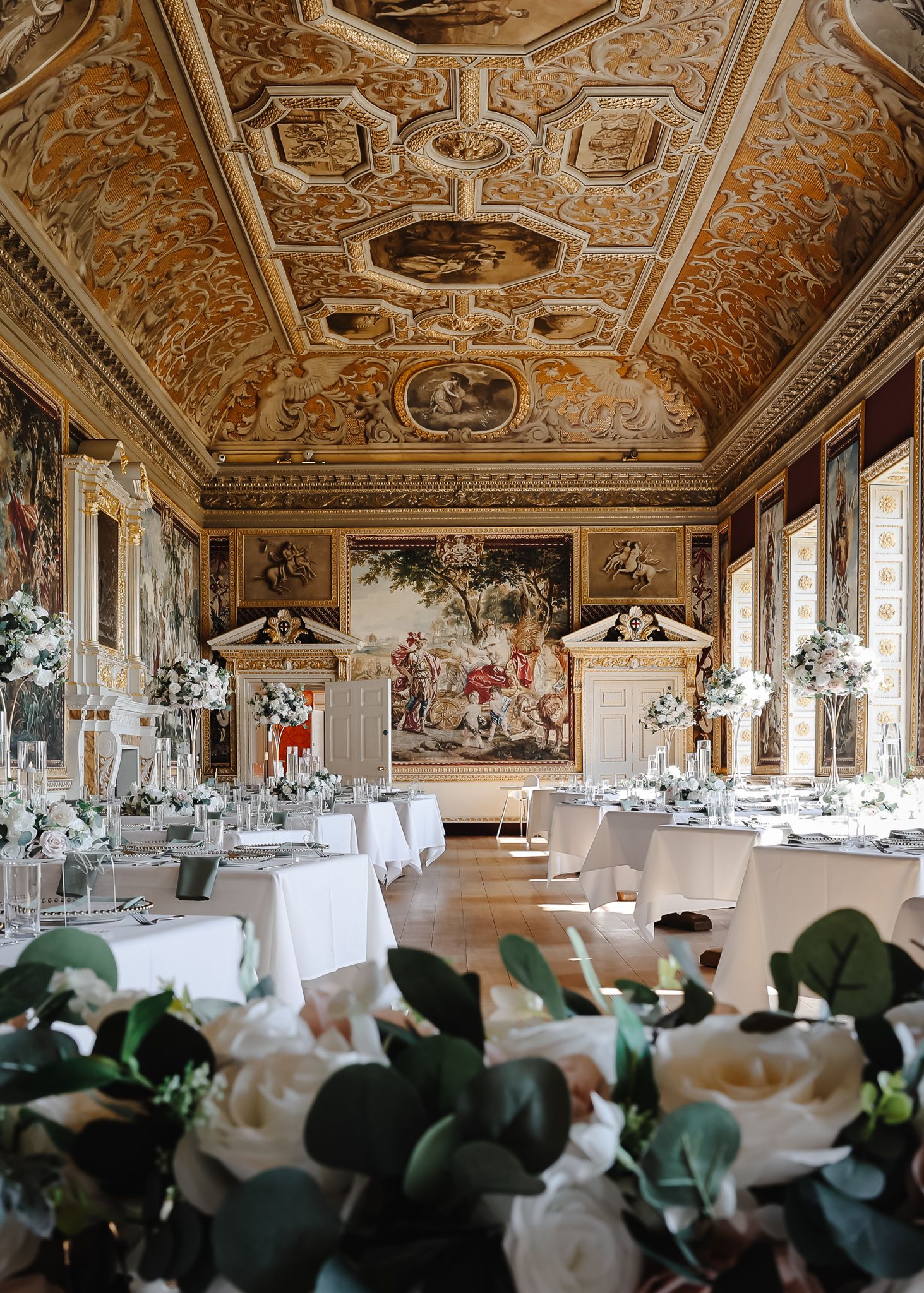 Elegant ballroom with ornate baroque ceiling frescoes and white-clothed dining tables set for a formal event.