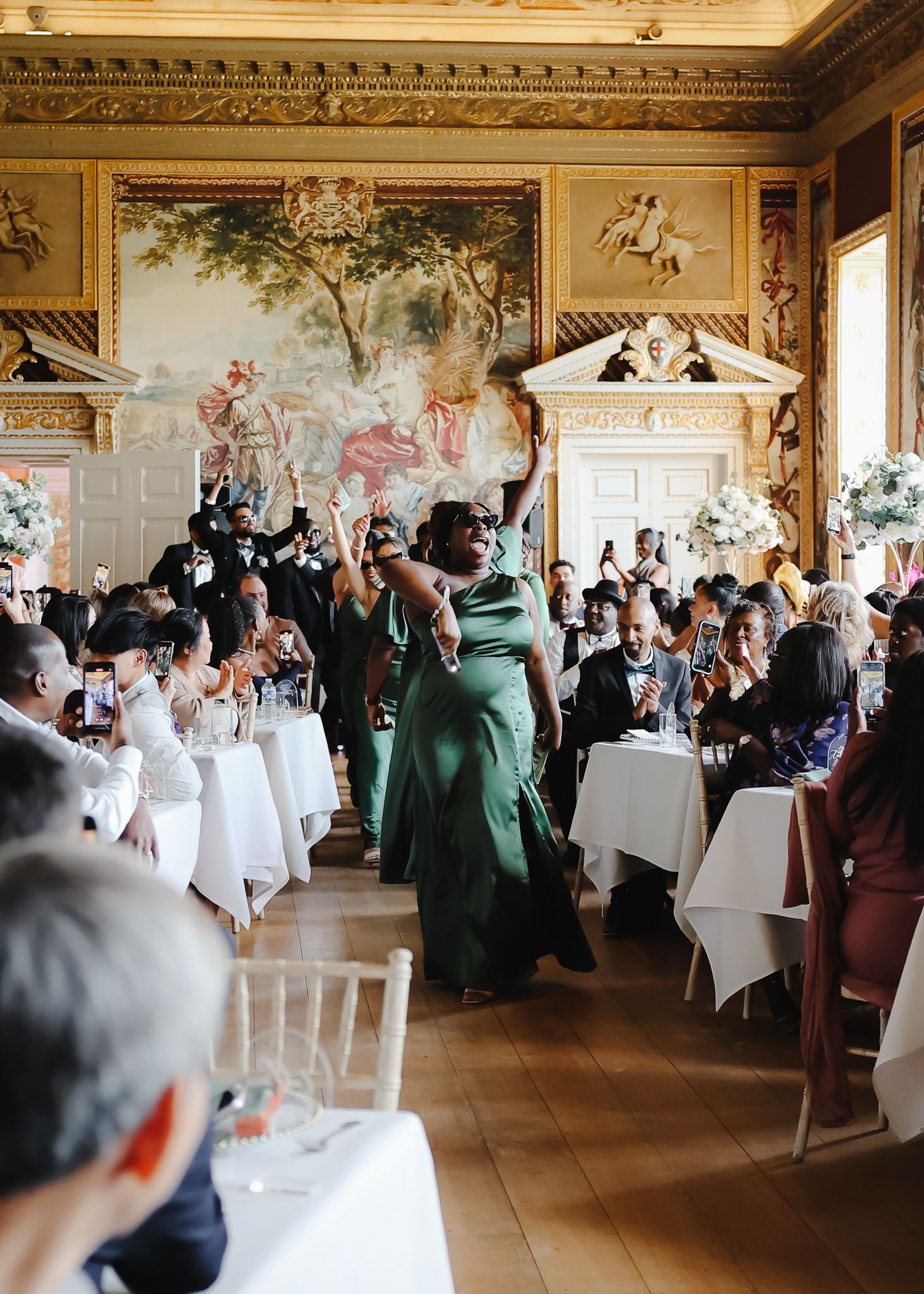 Elegant wedding reception setup in a grand ballroom with ornate ceiling and white-clothed tables filled with celebrating guests.