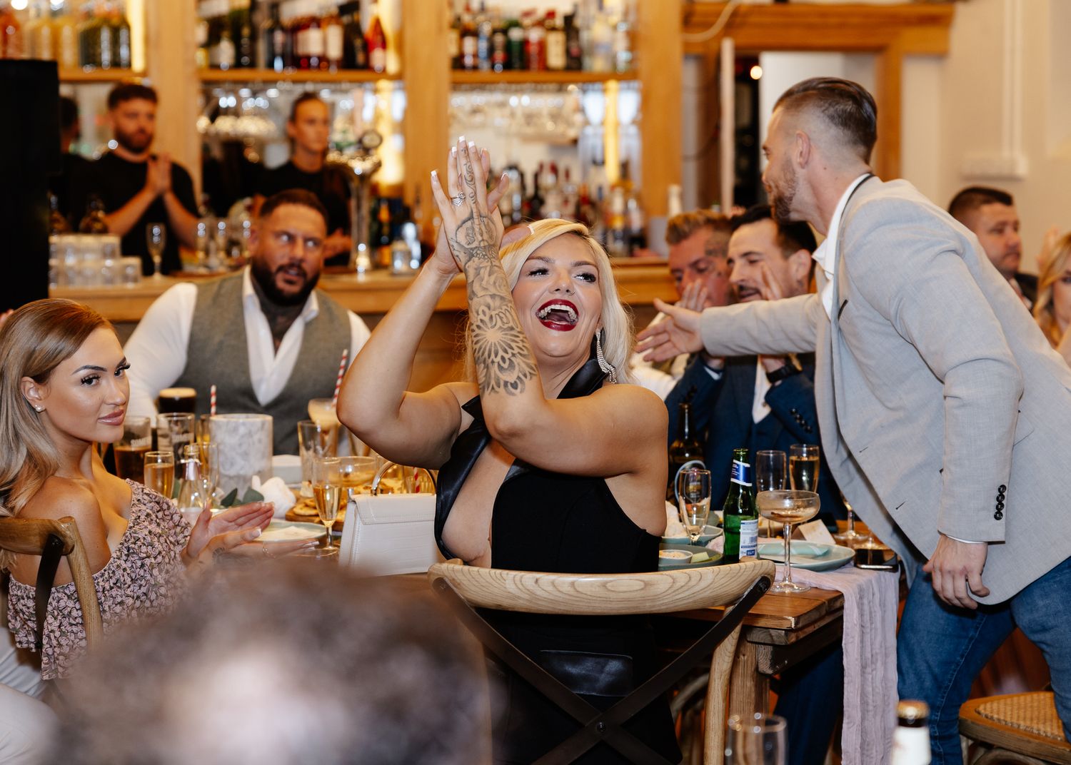 Guests enjoying drinks and lively conversation at a crowded bar with warm lighting and wooden decor.