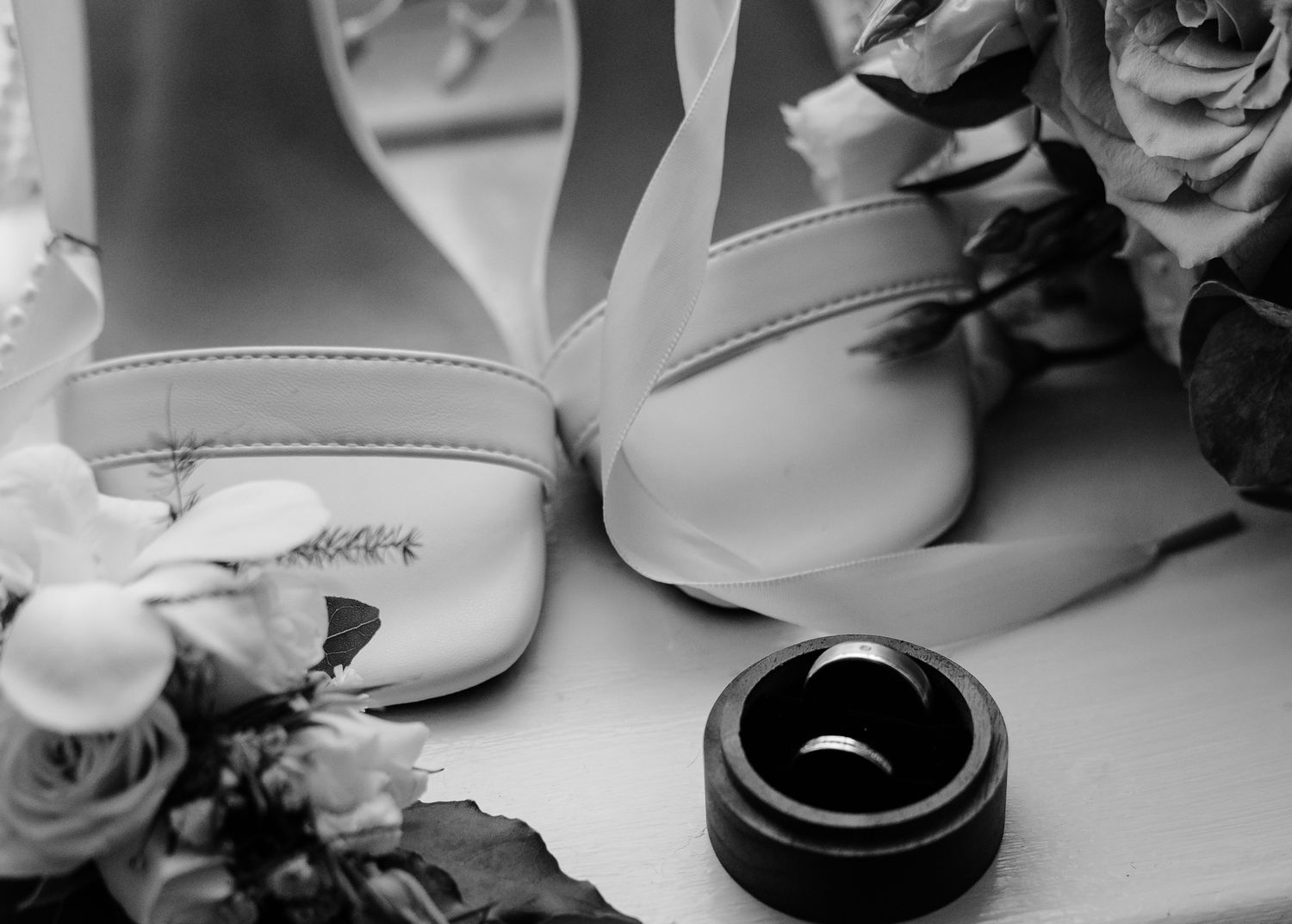 A black and white wedding photo showing wedding rings and floral decorations arranged on a table.