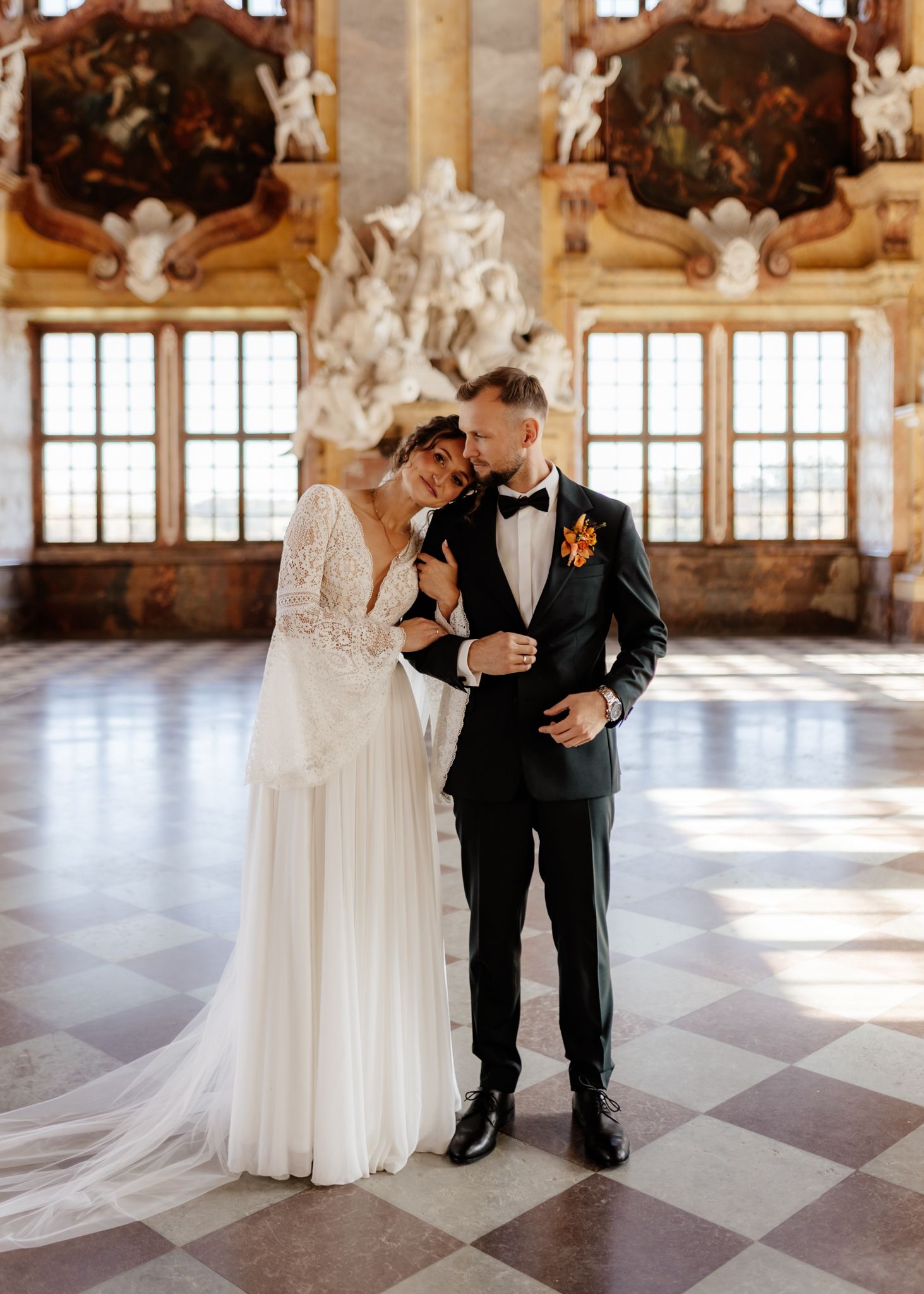 A romantic wedding moment in an ornate historic ballroom with checkered floors and baroque ceiling details.