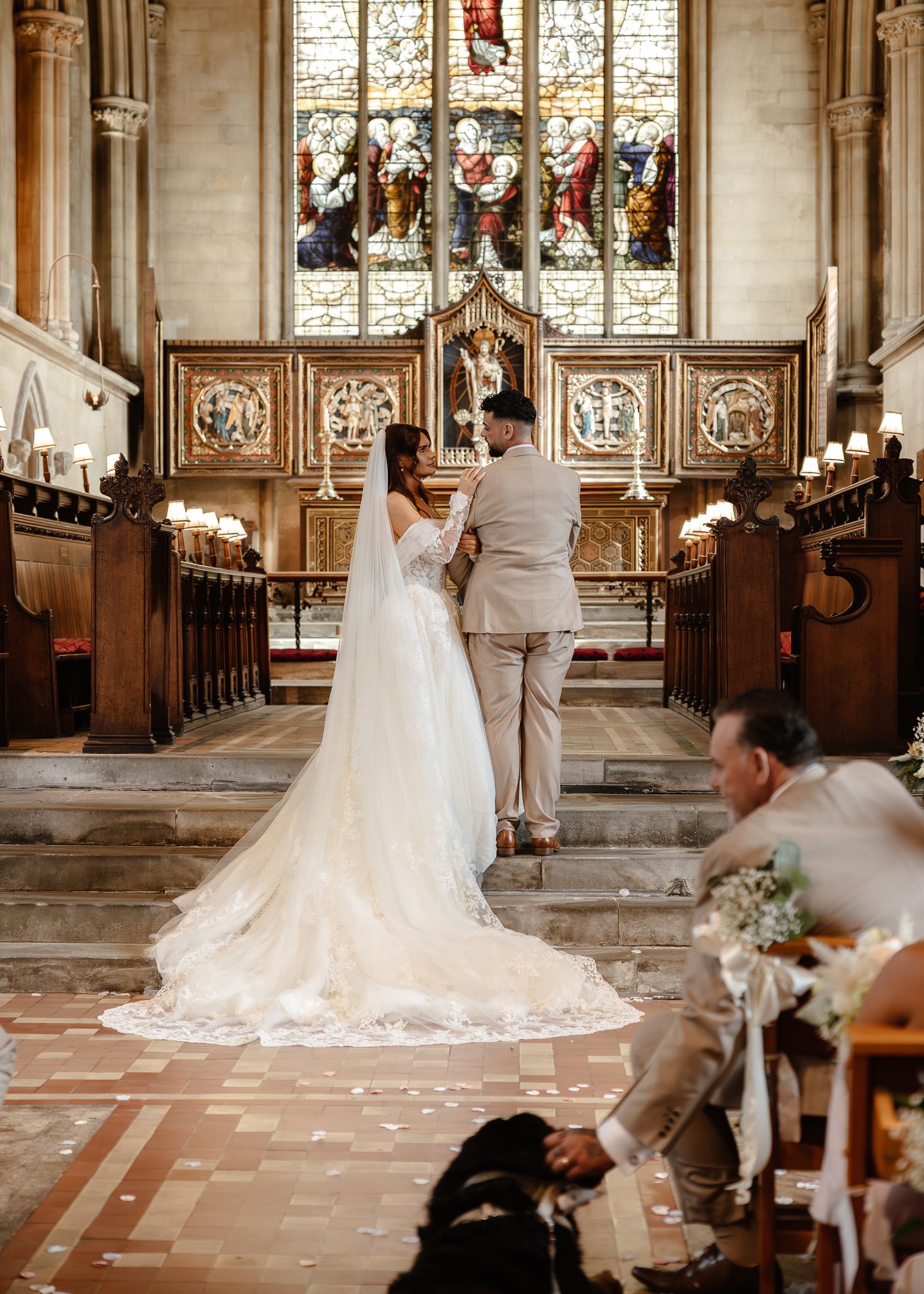 A couple stands together in a grand church with stained glass windows and ornate architectural details during their wedding ceremony.