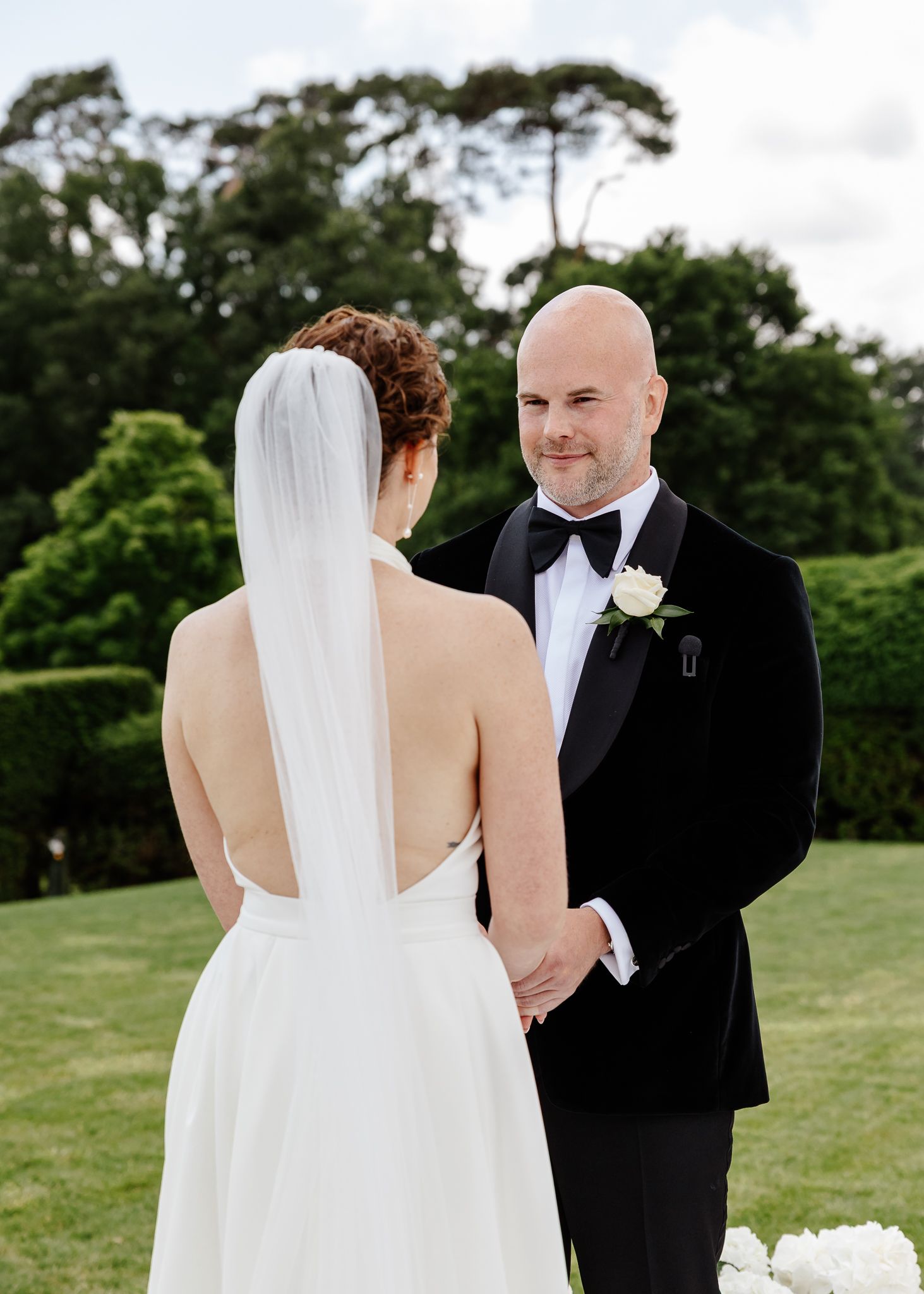 Elegant wedding ceremony on a manicured lawn with formal attire and classic white floral decor.