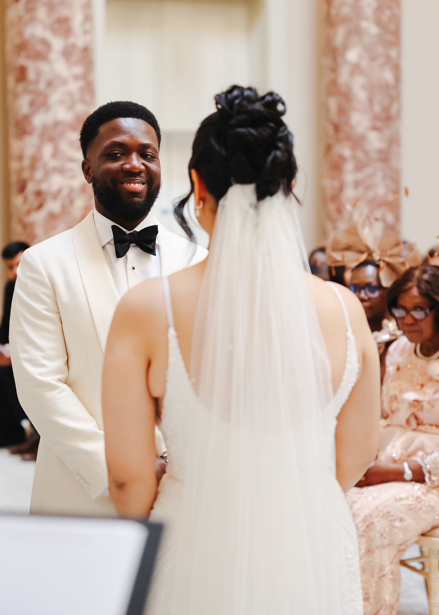 Wedding celebration in an ornate room with pink marble columns and elegant decor.