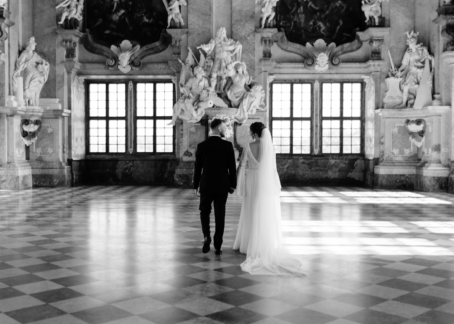 Newlywed couple dances in an elegant baroque palace hall with ornate frescoed walls and marble floors.