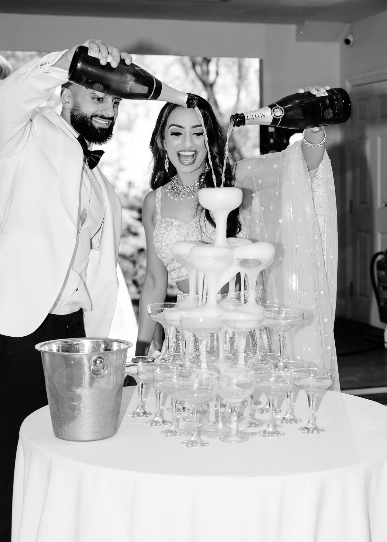 Celebratory moment pouring champagne into tower of glasses at elegant wedding reception.