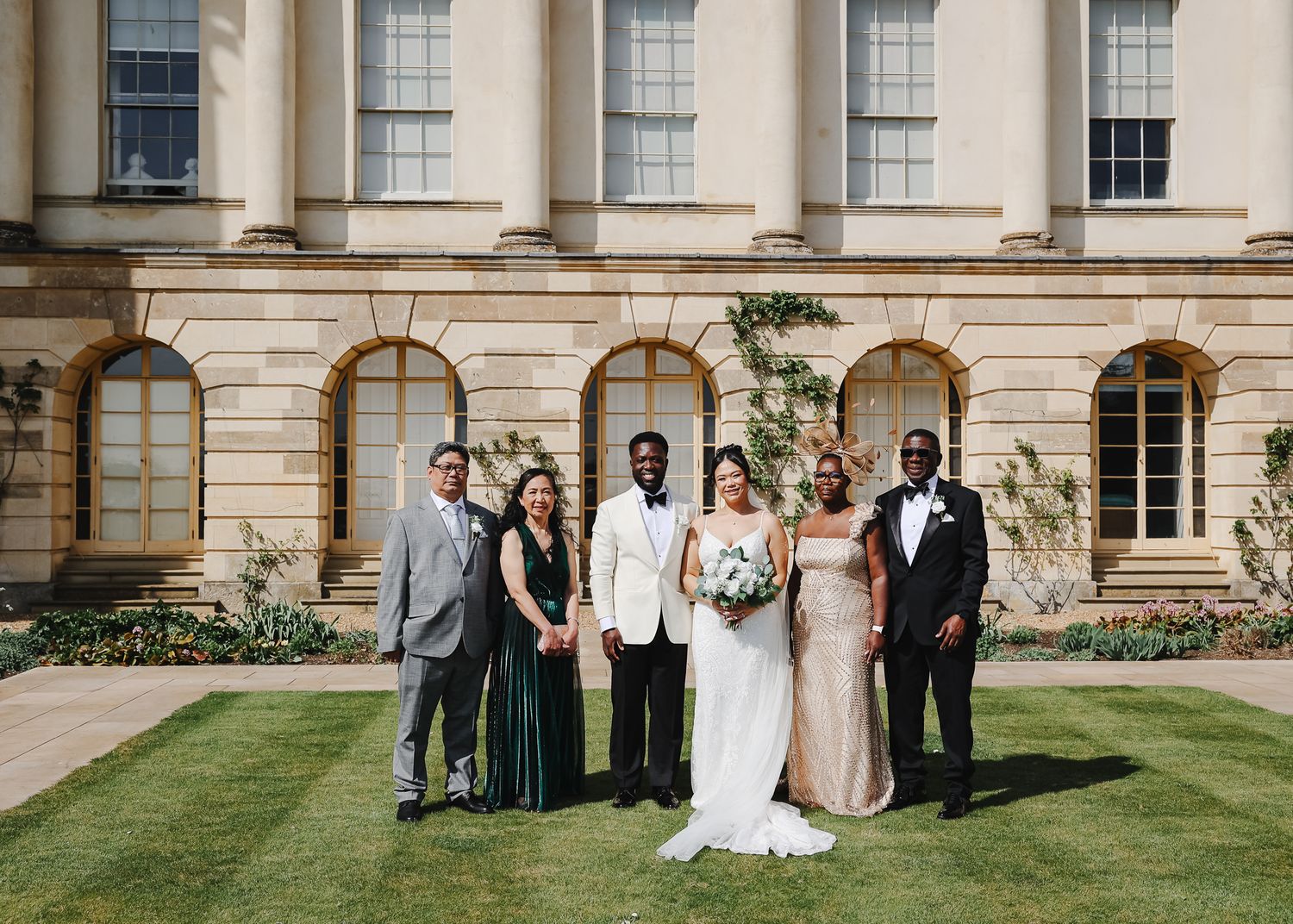 Wedding party poses in front of elegant stone building with classical architecture on sunny day.