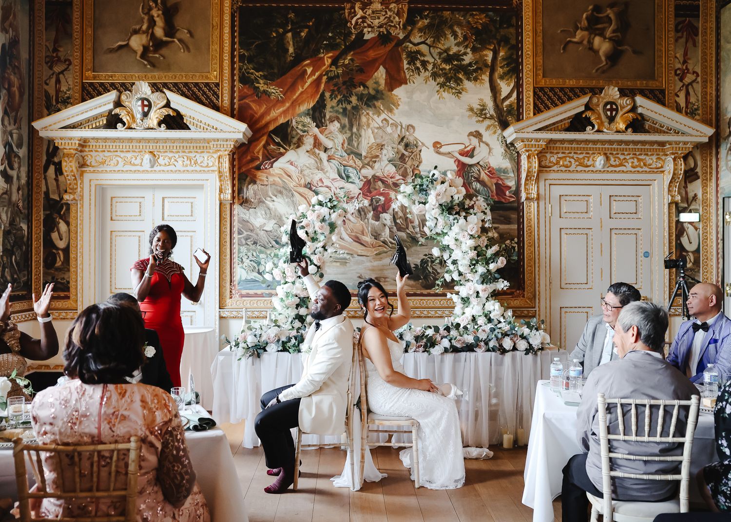 Elegant wedding celebration in an ornate ballroom with white floral arrangements and classical architectural details.