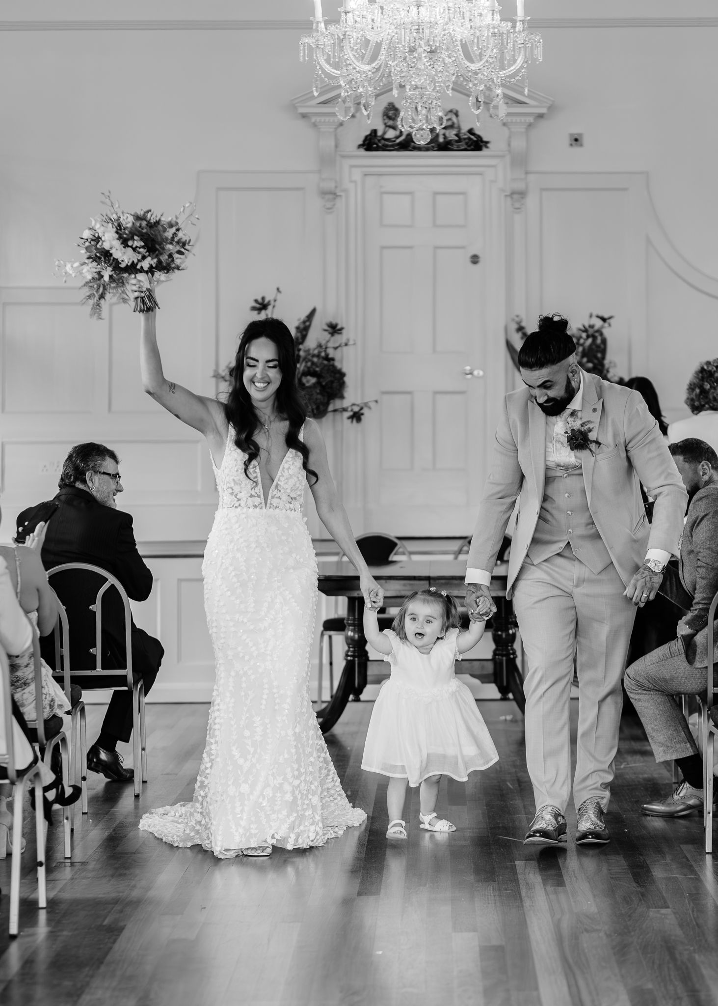 Wedding guests dance together on a wooden floor beneath elegant chandeliers during a reception celebration.