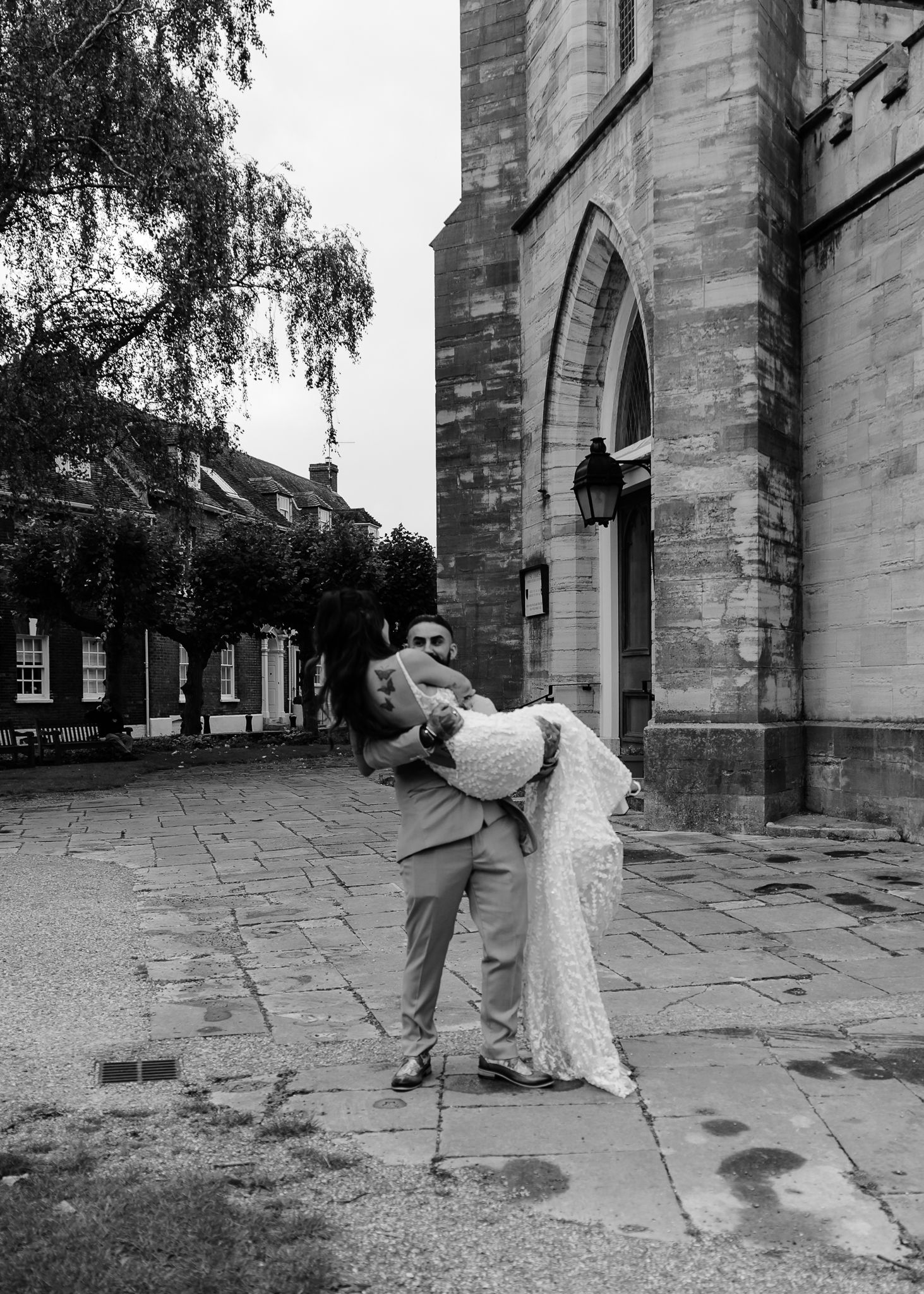 A series of black and white photos showing a couple in vintage attire posing playfully against a stone church wall.