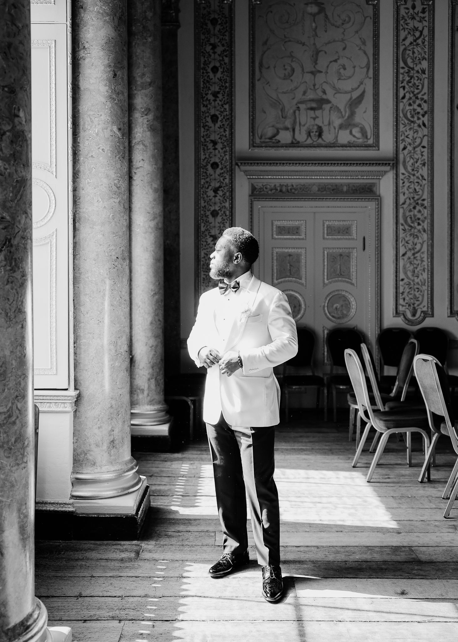 Black and white photograph showing legs and feet of people walking along a columned corridor in a formal setting.