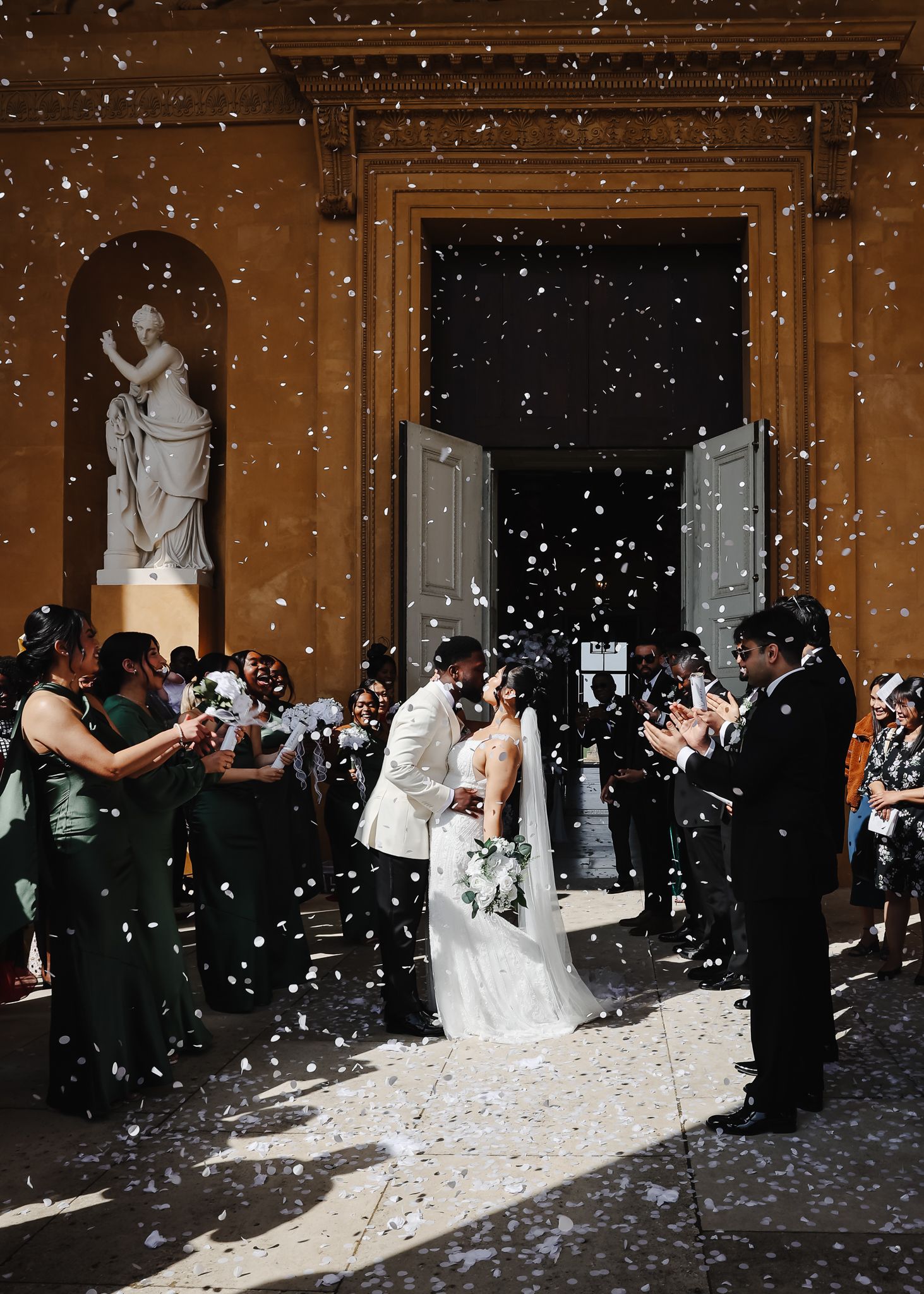 A sequence of wedding celebration photos showing guests throwing white confetti in an elegant indoor venue with classical statues.