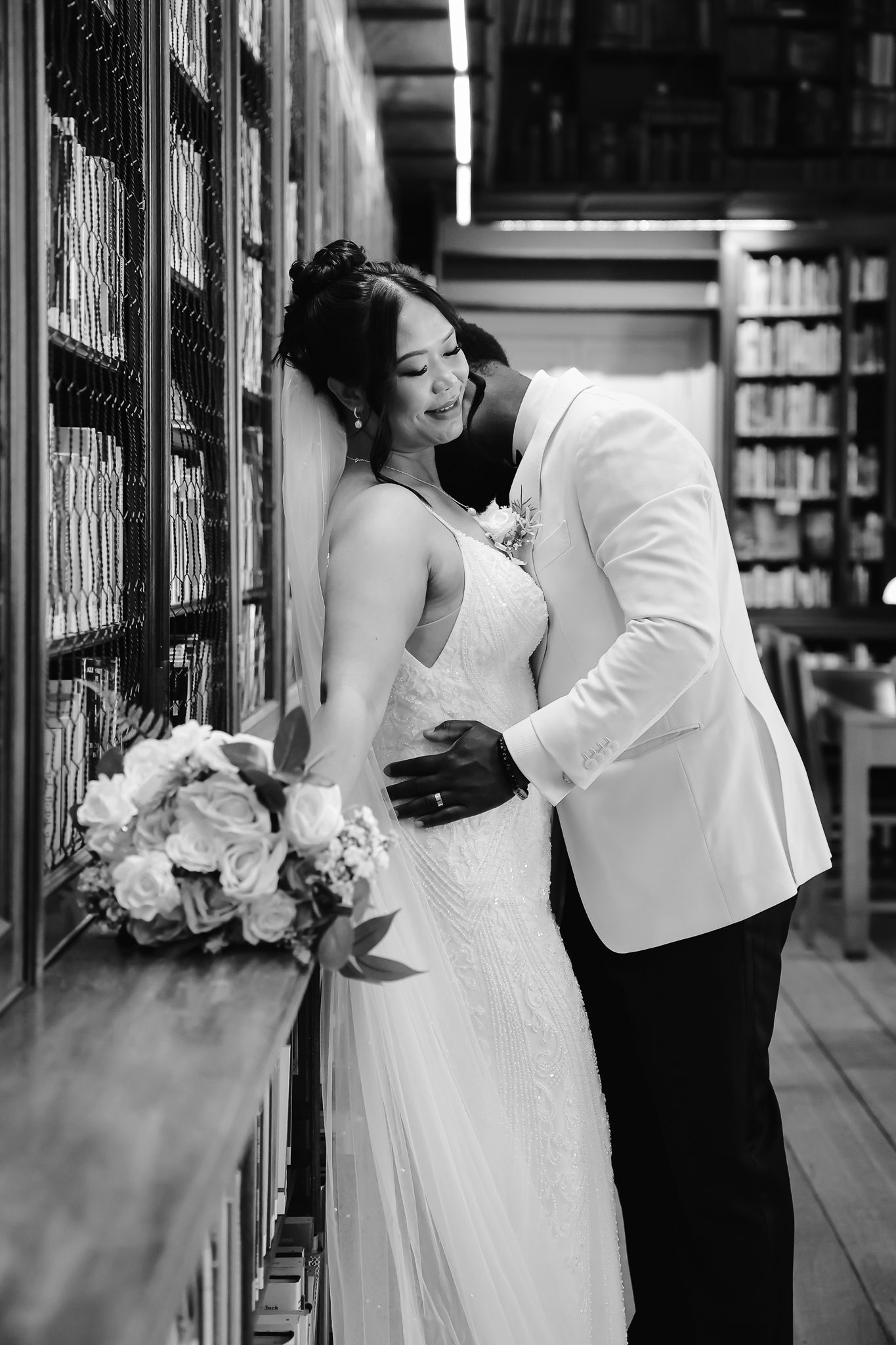 Black and white wedding photos taken in a library with bookshelves creating a romantic backdrop.