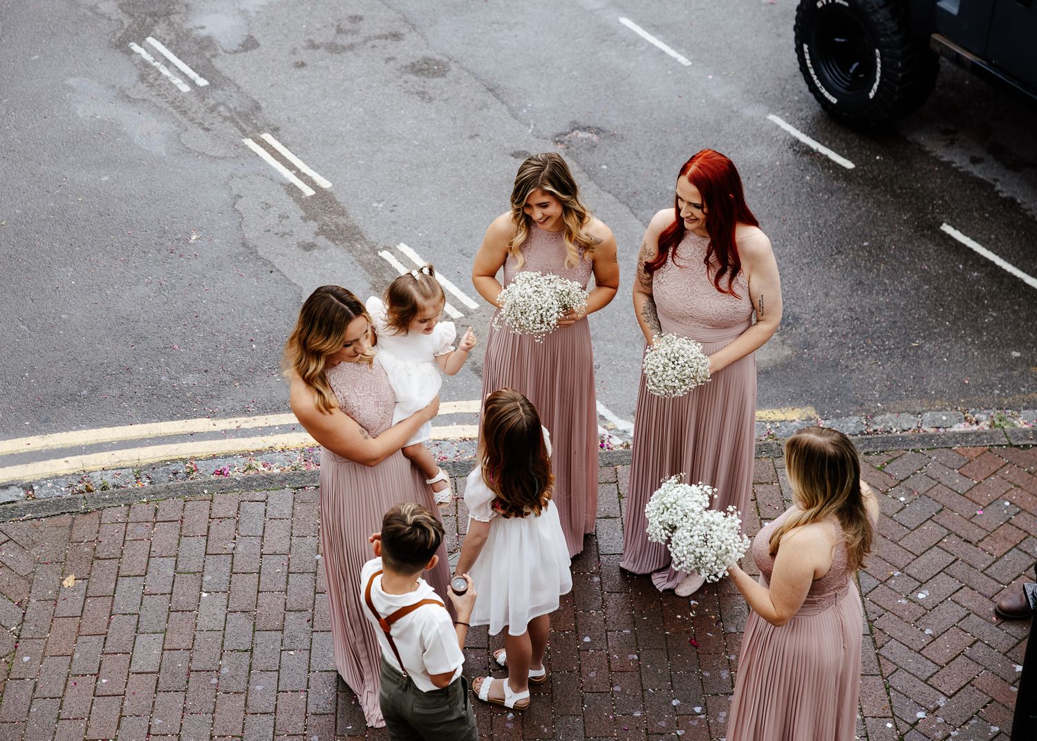 Wedding party walking down cobblestone street in formal attire with bridesmaids in dusty rose dresses.