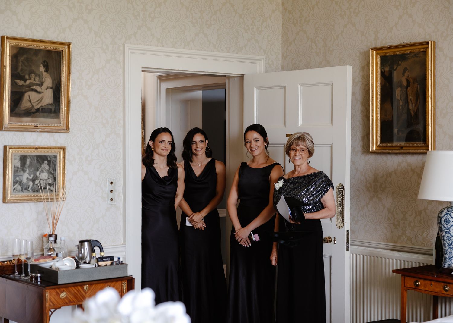 A panoramic view of a formal event room with framed photos on walls and people in black dresses gathered together.