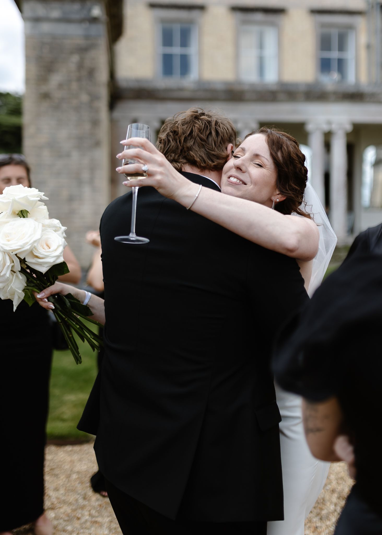 A joyful couple embraces and celebrates with champagne glasses and white flowers at an elegant outdoor venue.
